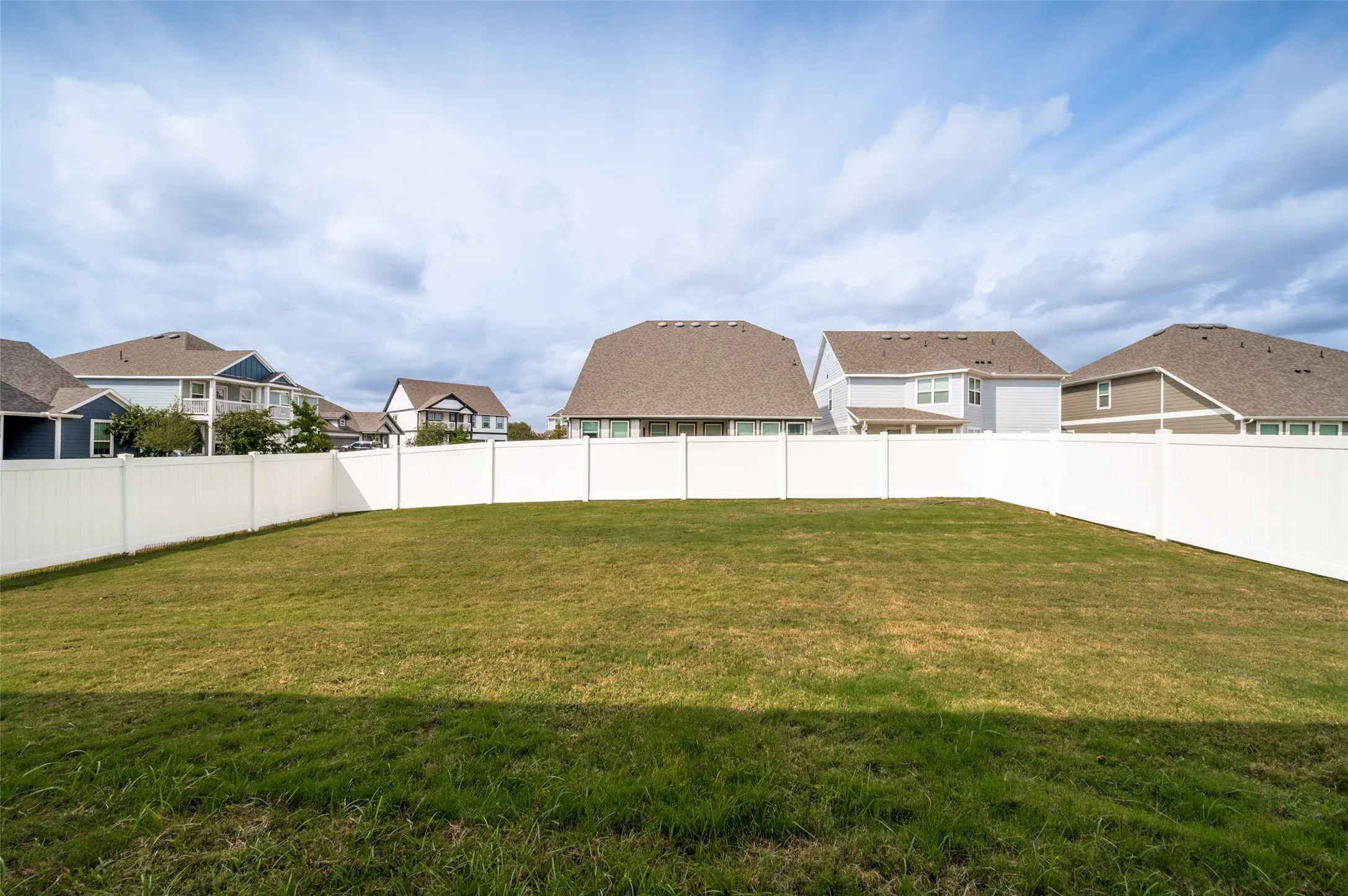 Expansive grassy area with a white privacy fence