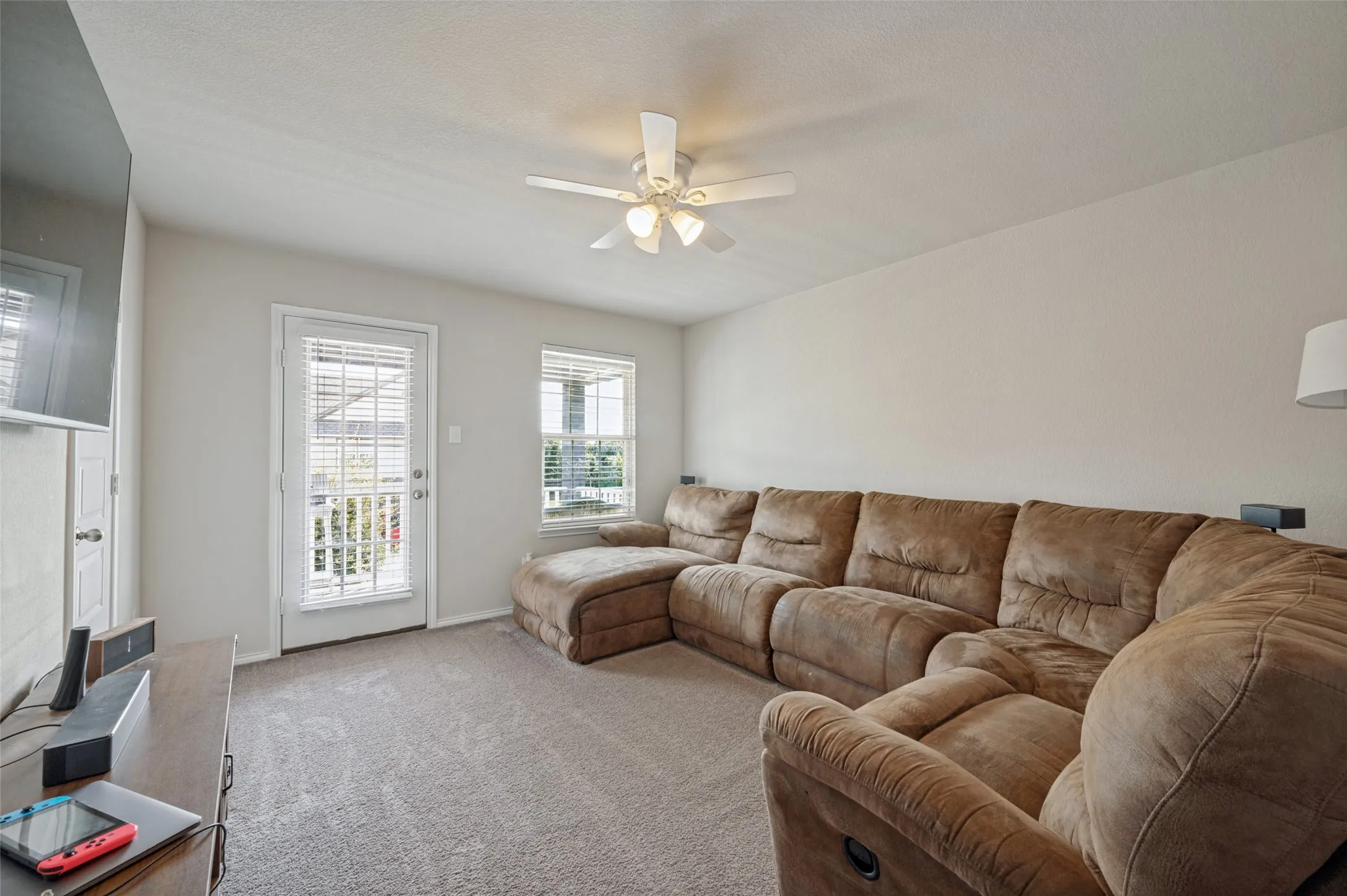 Carpeted flooring, ceiling fan, white paneled door, and two windows with blinds