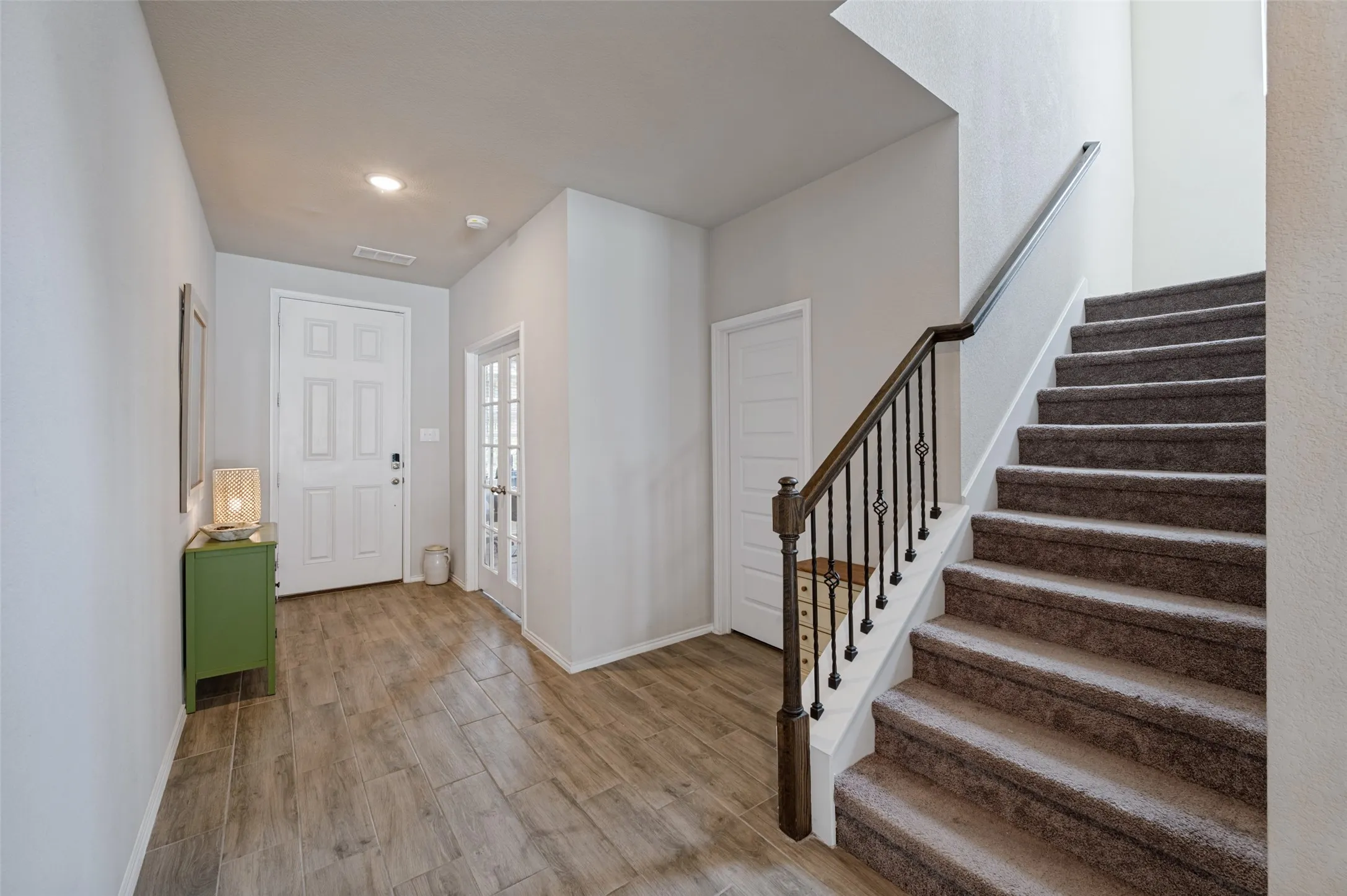 Entryway featuring wood-finish flooring, recessed lighting, white paneled doors, and a carpeted staircase with wrought iron balusters