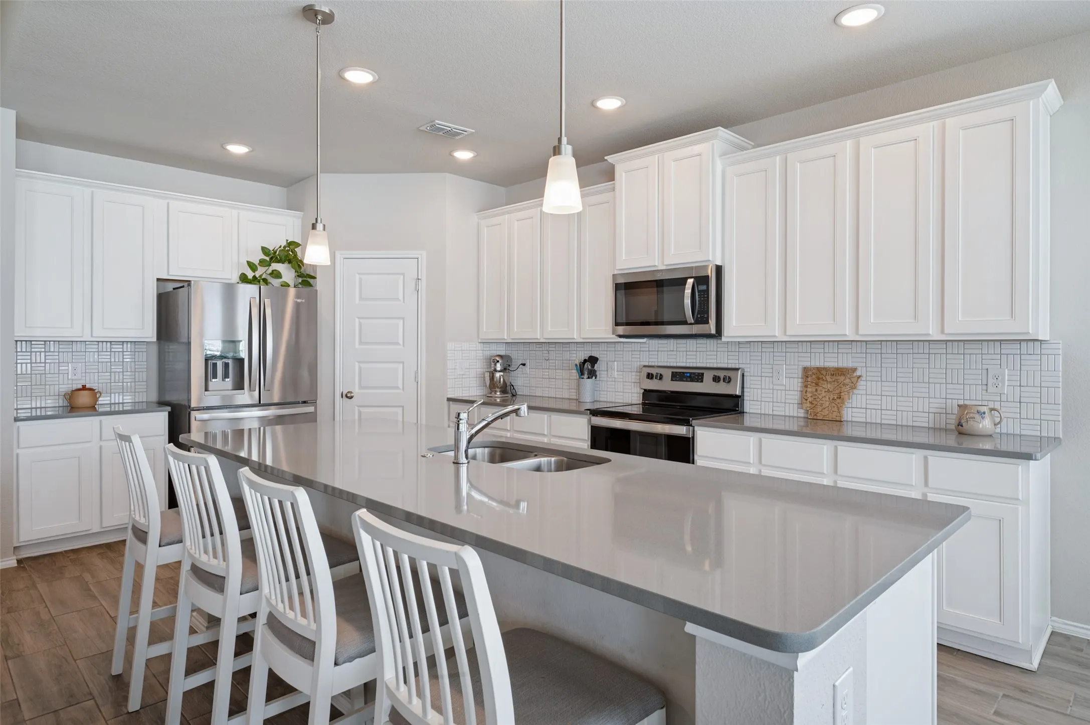 Kitchen featuring a spacious island with an integrated sink, stainless steel appliances, white cabinetry, recessed lighting, and wood-finish flooring