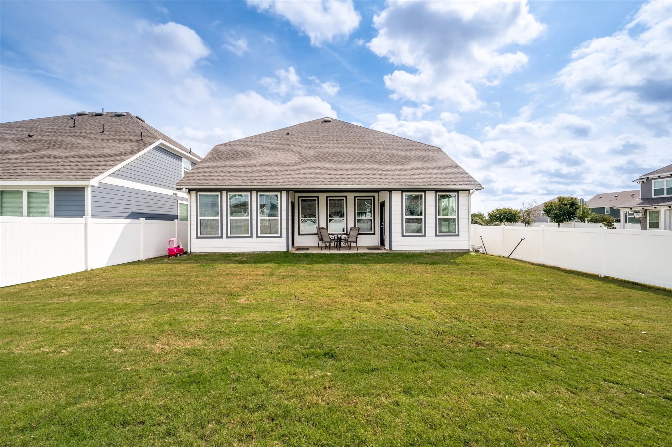 Spacious backyard with a grass lawn, white privacy fencing, and a concrete patio