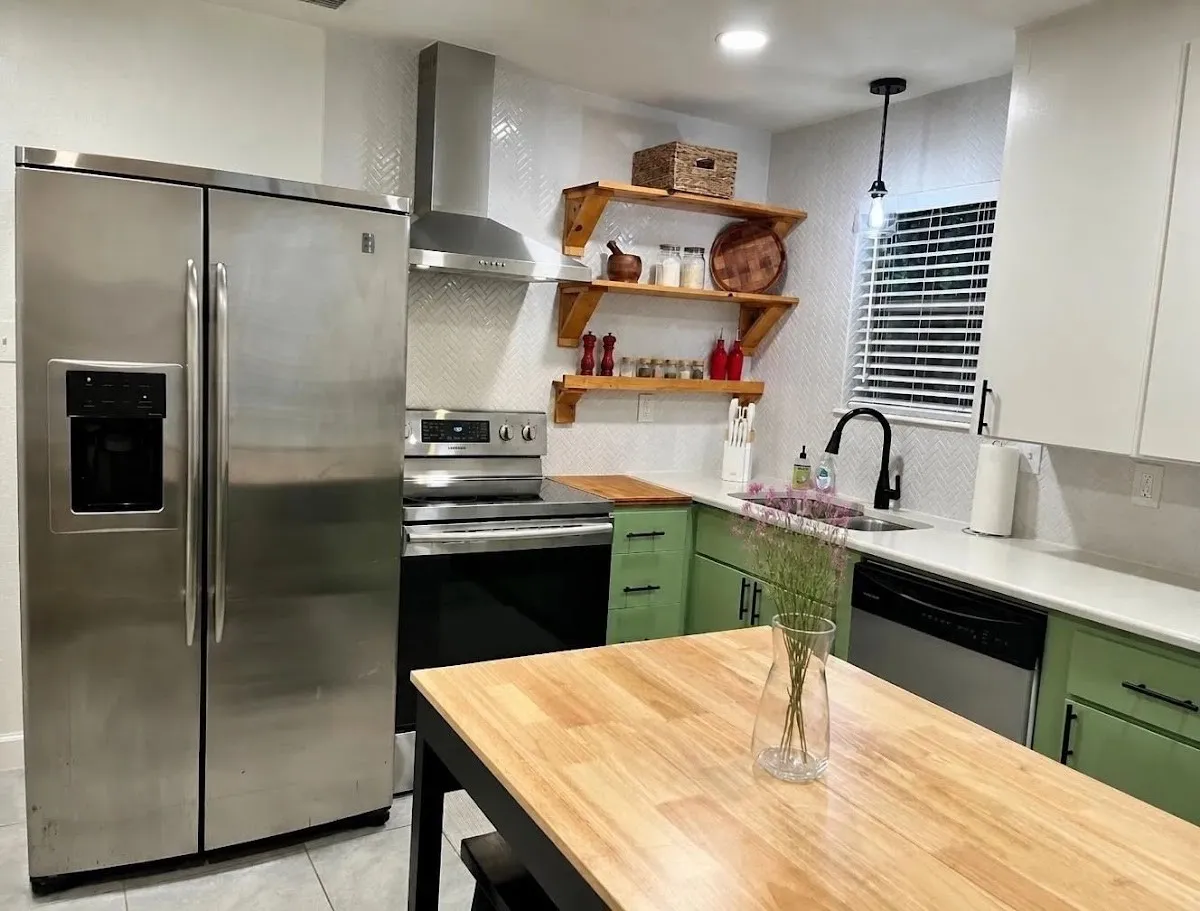 Stainless steel appliances, white quartz countertops, green and white cabinetry, wood-finish open shelving, and a wood-finish island