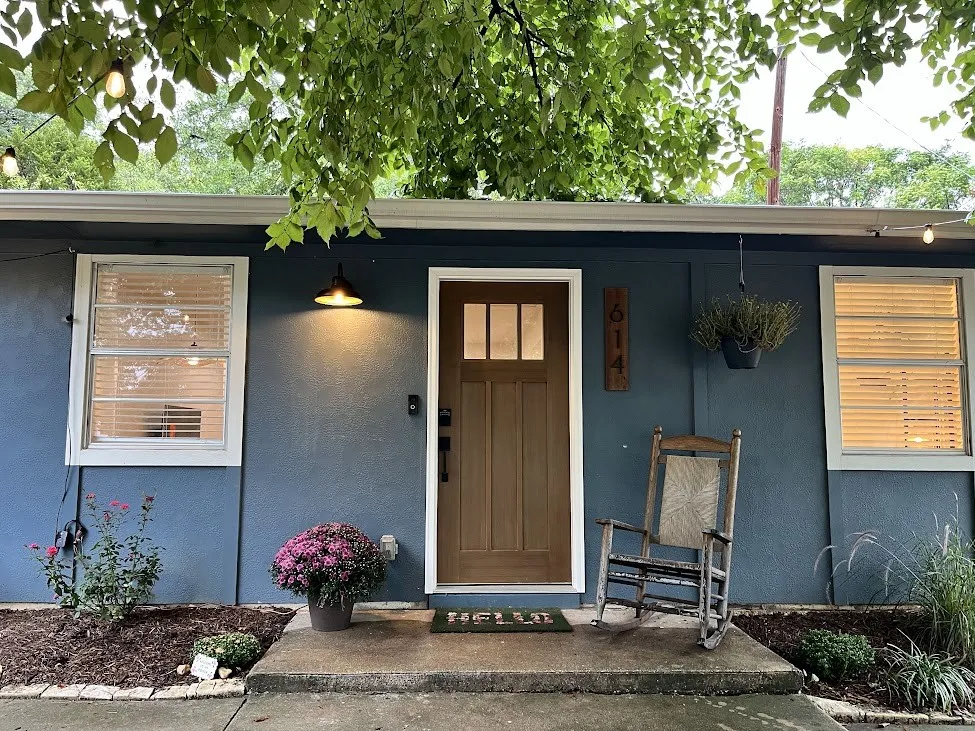 Blue exterior with white trim, wood-finish front door with glass lites, concrete porch, and exterior wall light