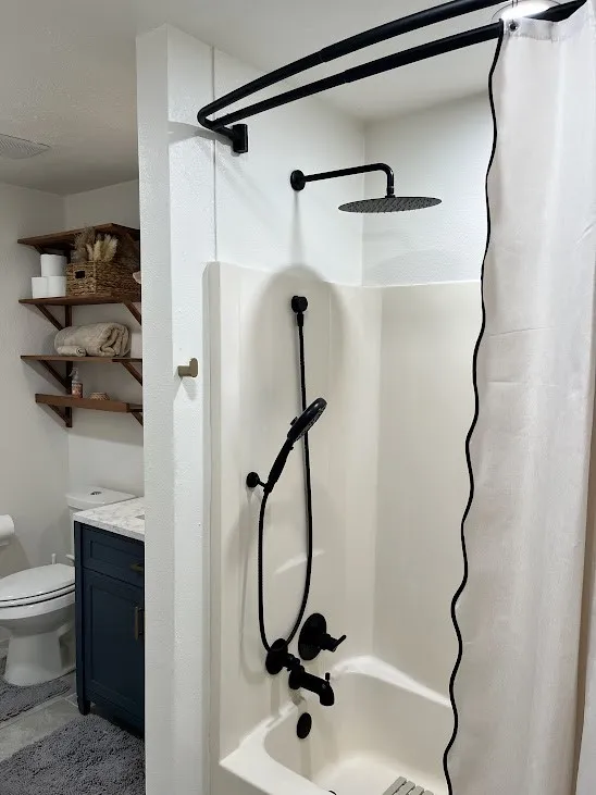 Bathtub with black-finish shower fixtures, rainfall showerhead, and handheld sprayer