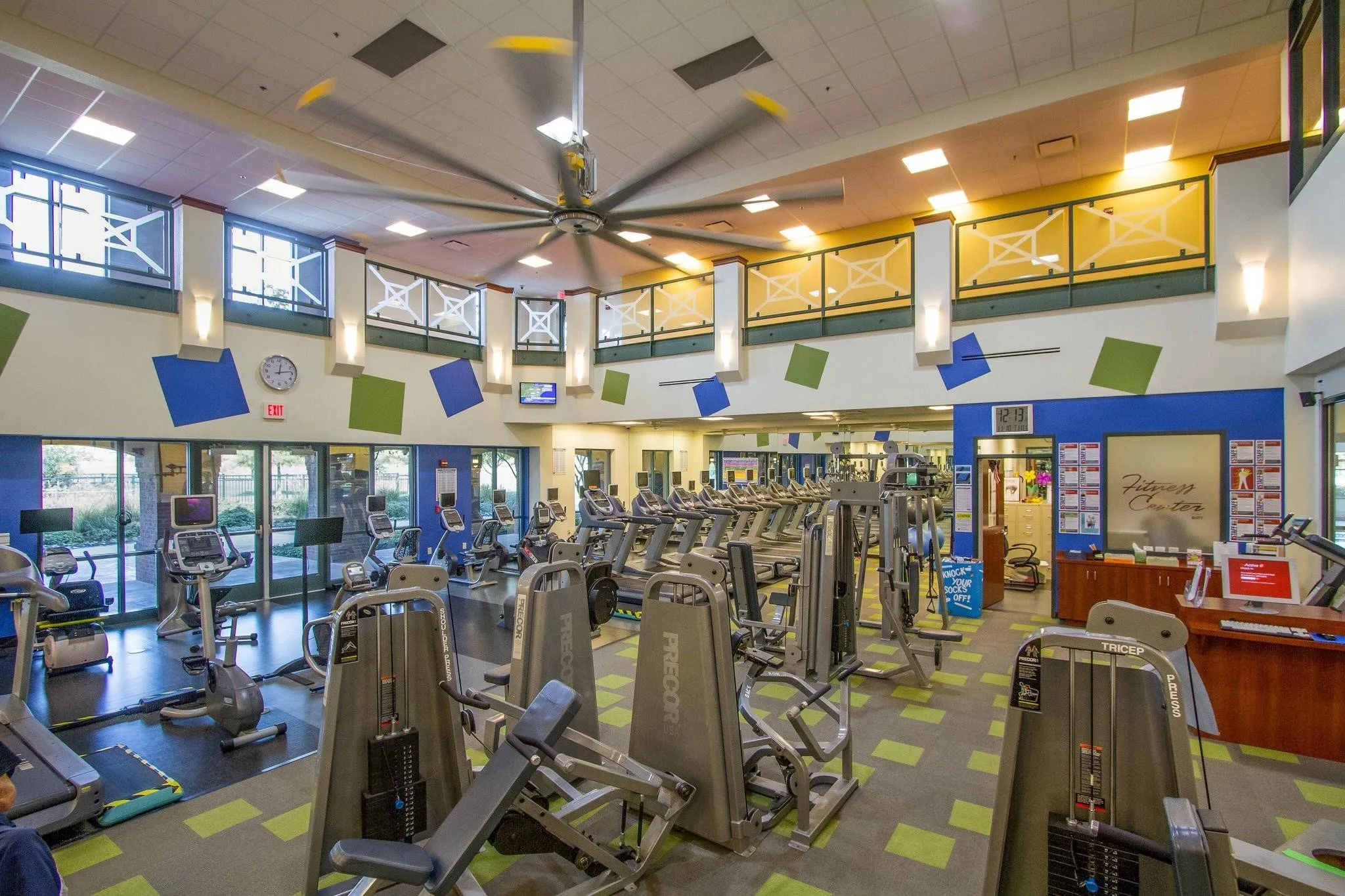 Spacious fitness center featuring a large ceiling fan, extensive exercise equipment, transom windows, and patterned flooring