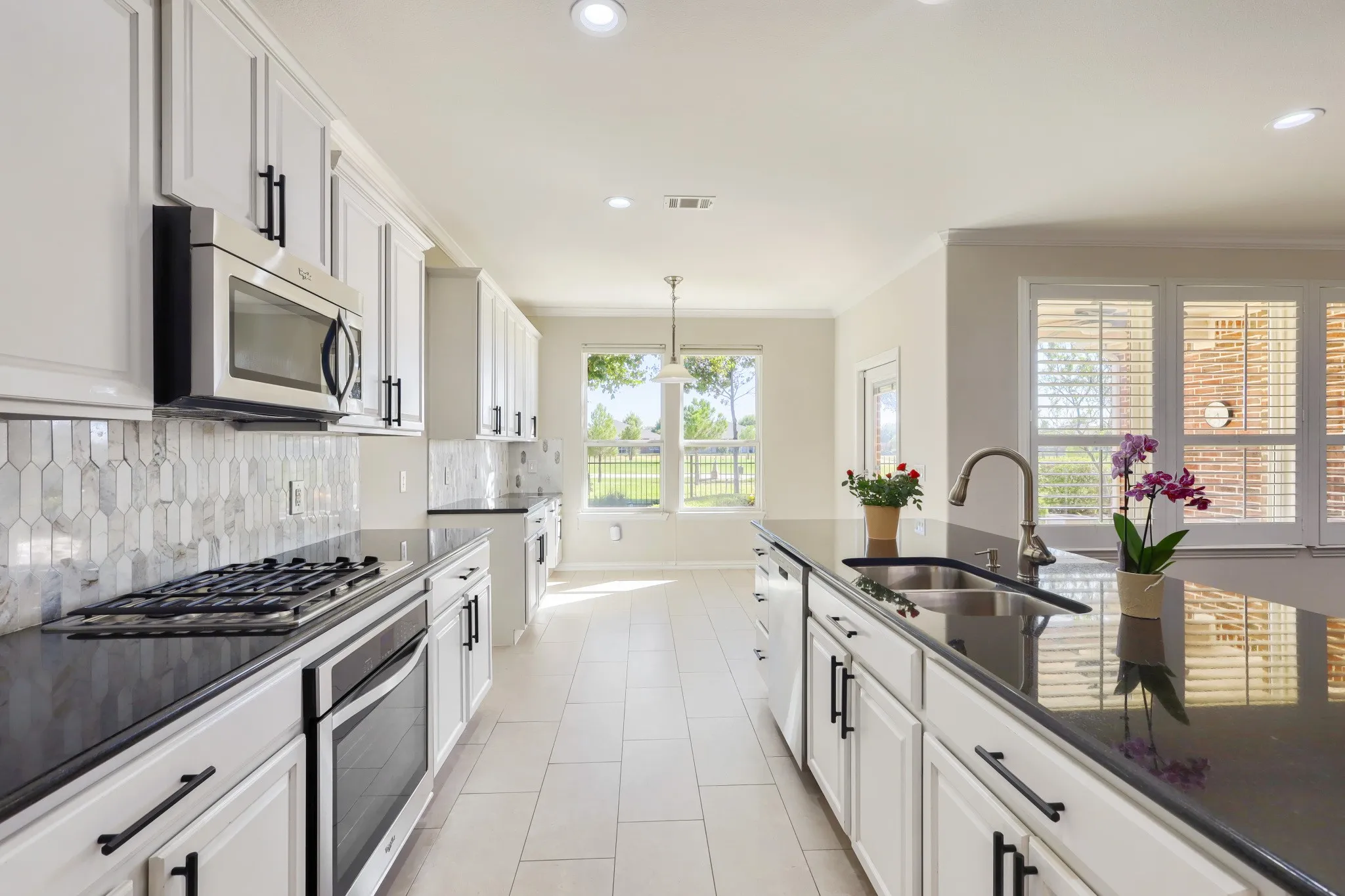 Kitchen featuring white shaker cabinetry, black countertops, stainless steel appliances, a tile backsplash, and light tile flooring