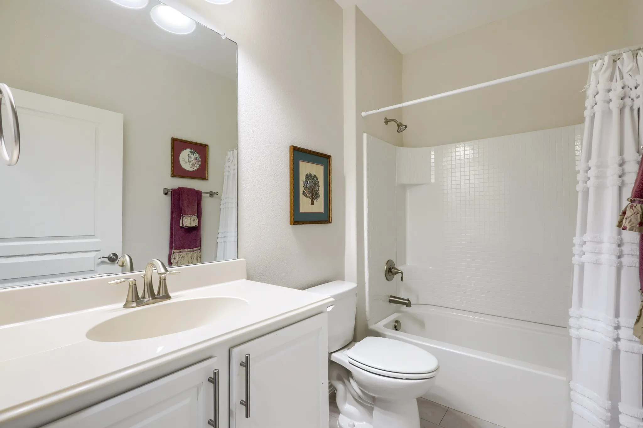 White vanity with integrated sink, brushed nickel faucet, large mirror, and overhead lighting