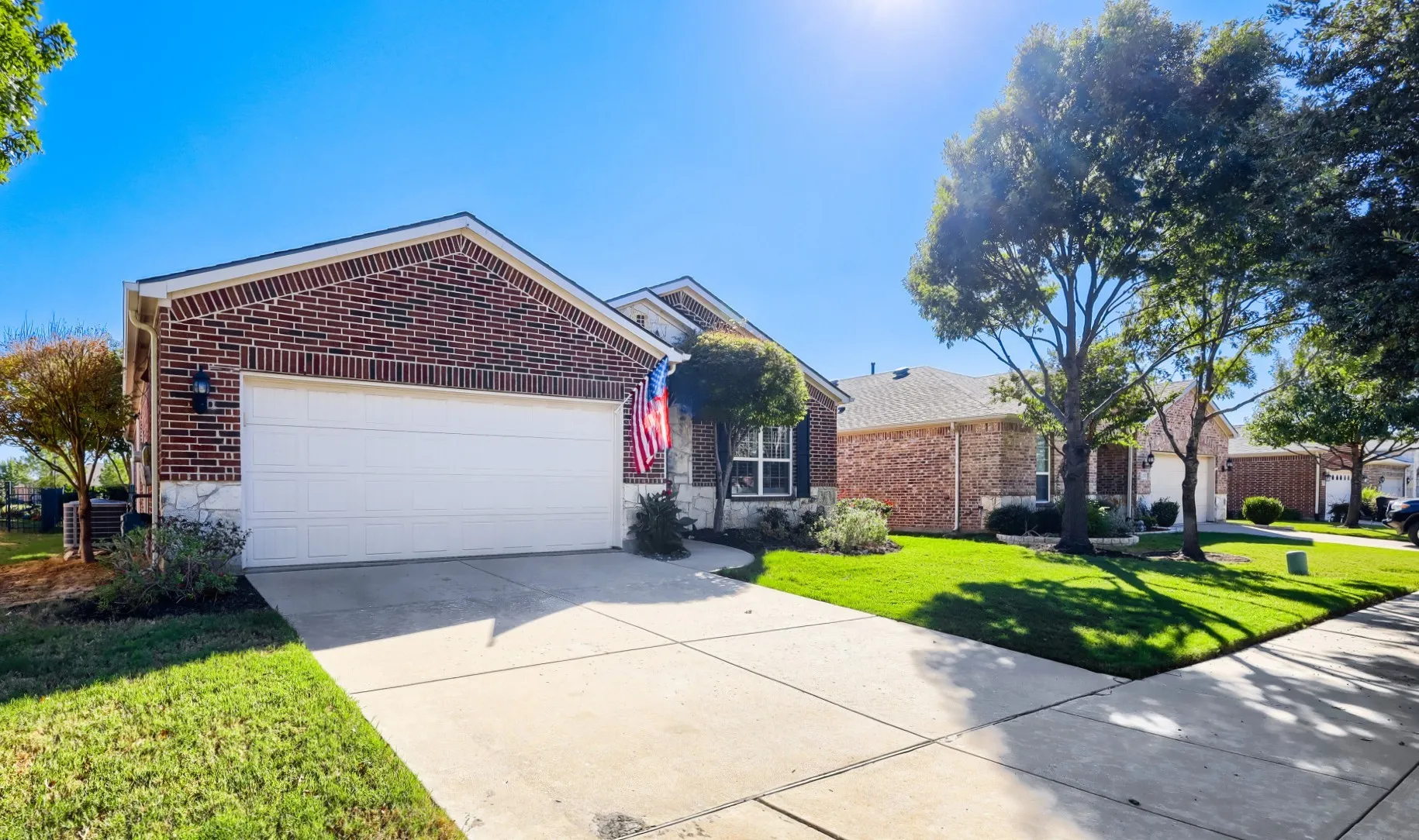 Brick exterior with stone accents, attached garage, concrete driveway, and established trees