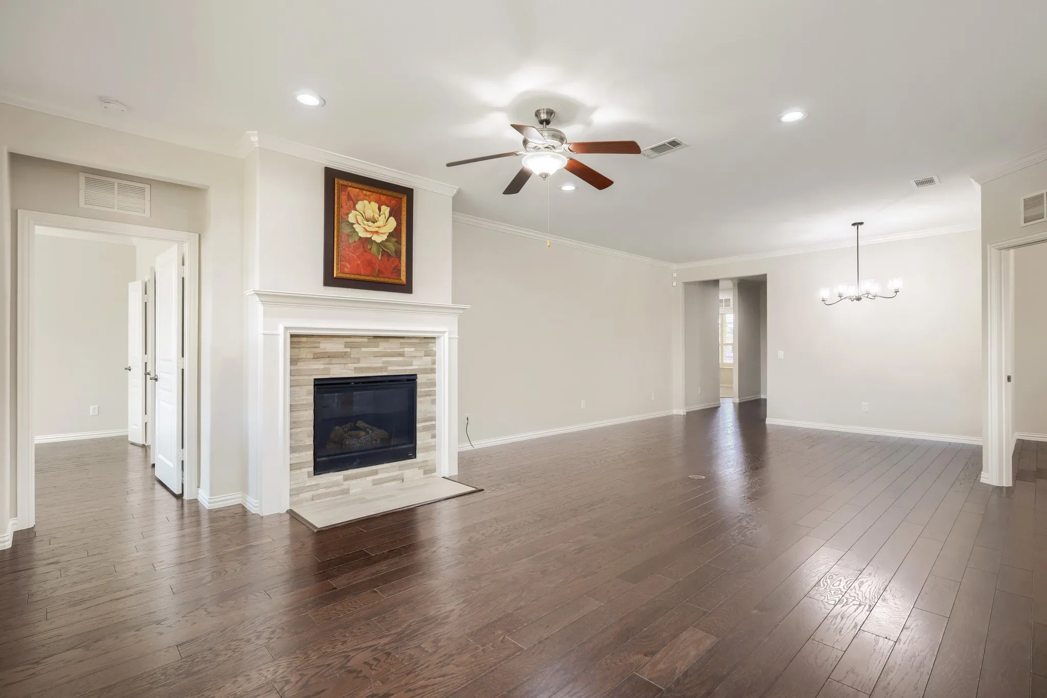 Hardwood flooring throughout, a gas fireplace with a stacked stone surround and white mantel, a ceiling fan with integrated lighting, recessed lighting, and a chandelier