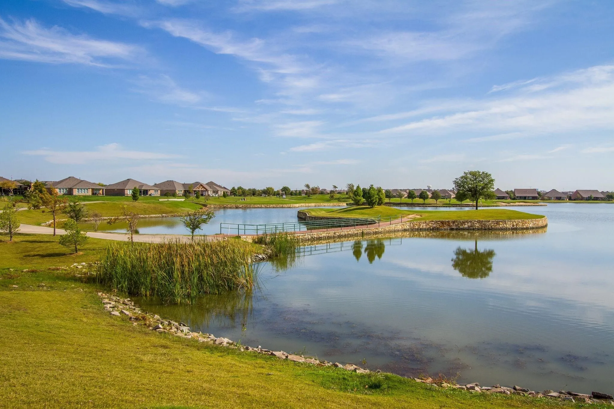 Expansive lake with a stone-edged island, surrounded by manicured lawns and mature trees