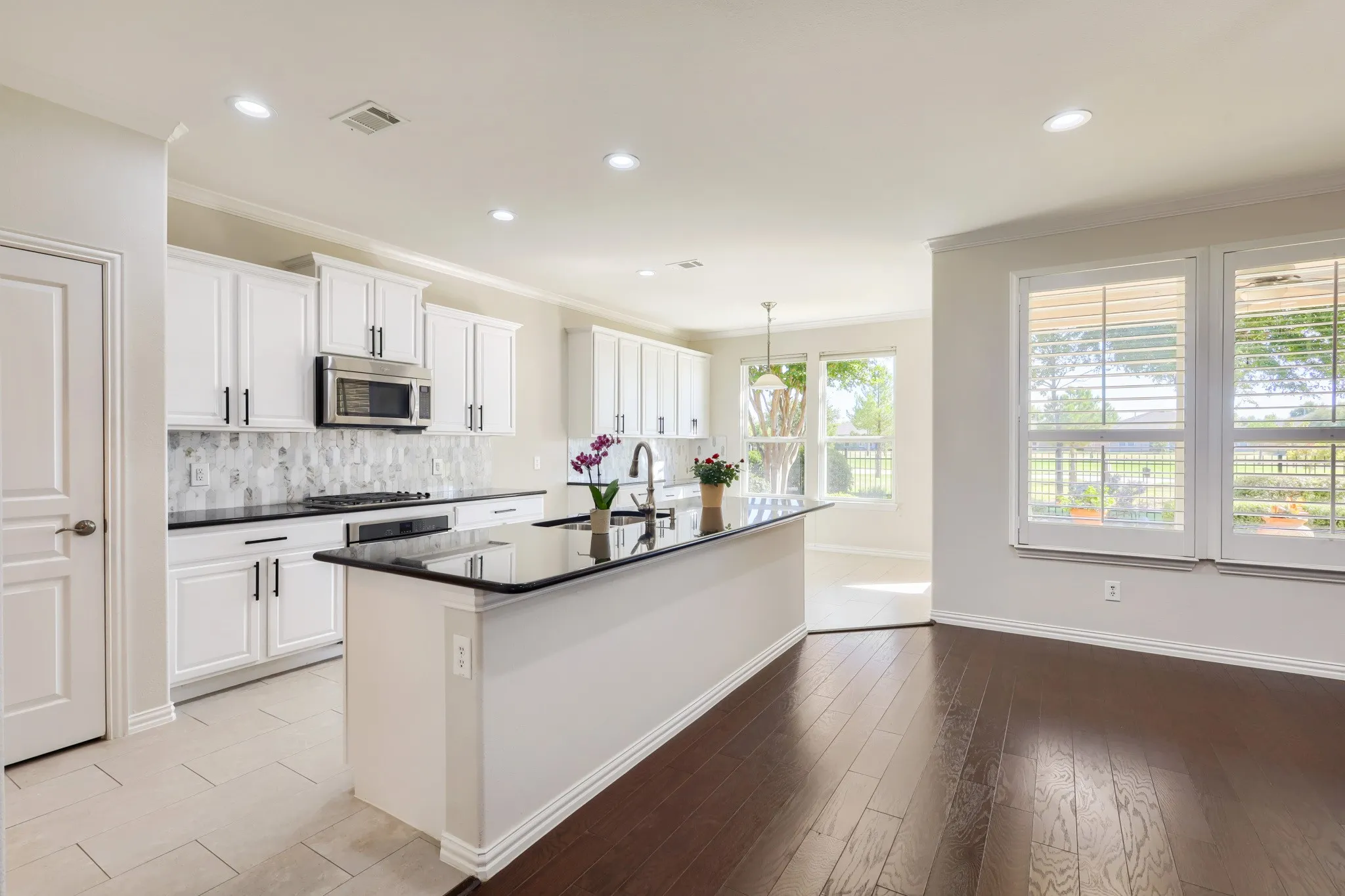 Kitchen featuring white cabinetry, a dark countertop island, stainless steel microwave, and tile backsplash