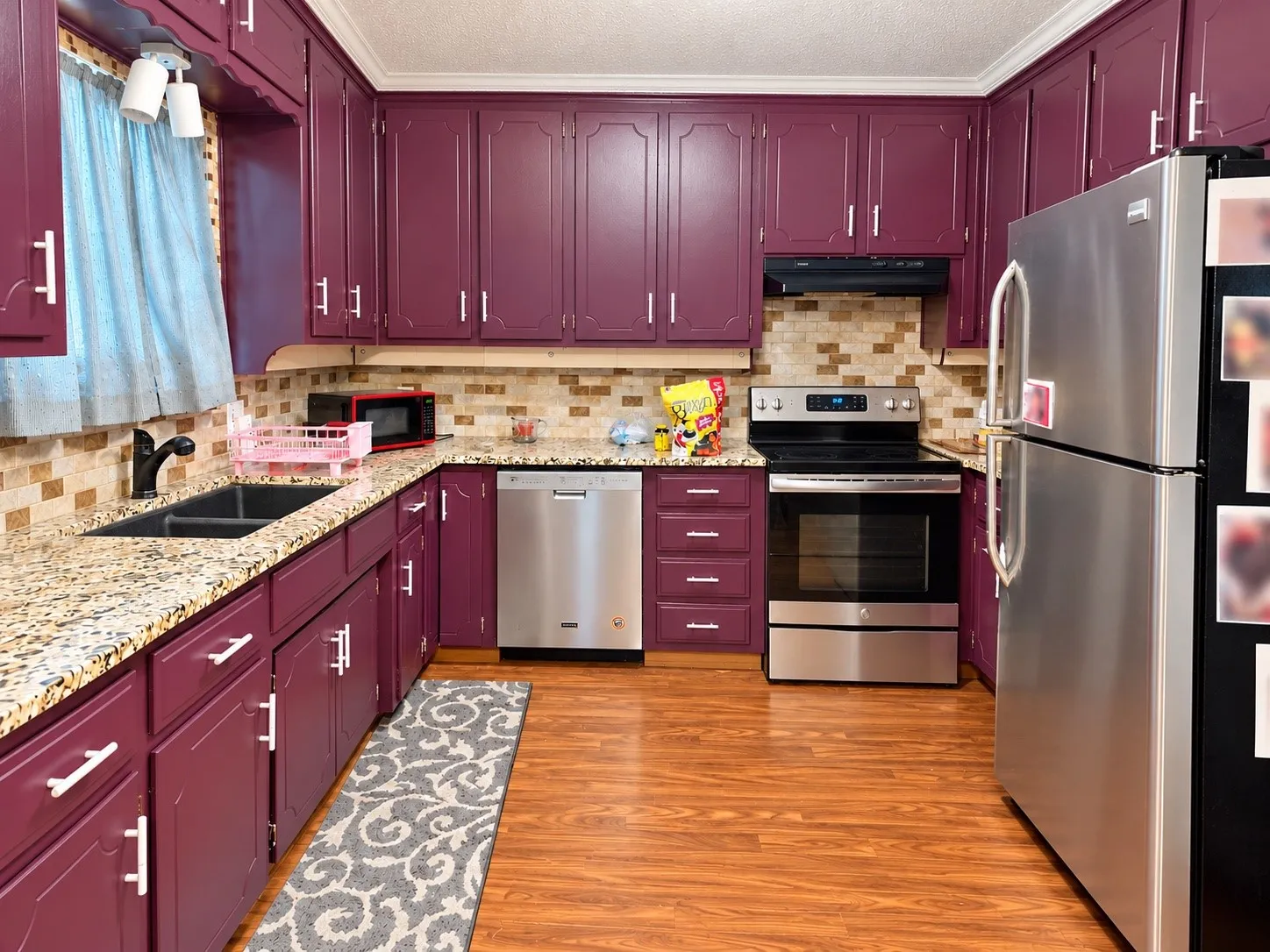 Kitchen featuring rich plum-toned cabinetry, light-toned granite countertops, and a mosaic tile backsplash