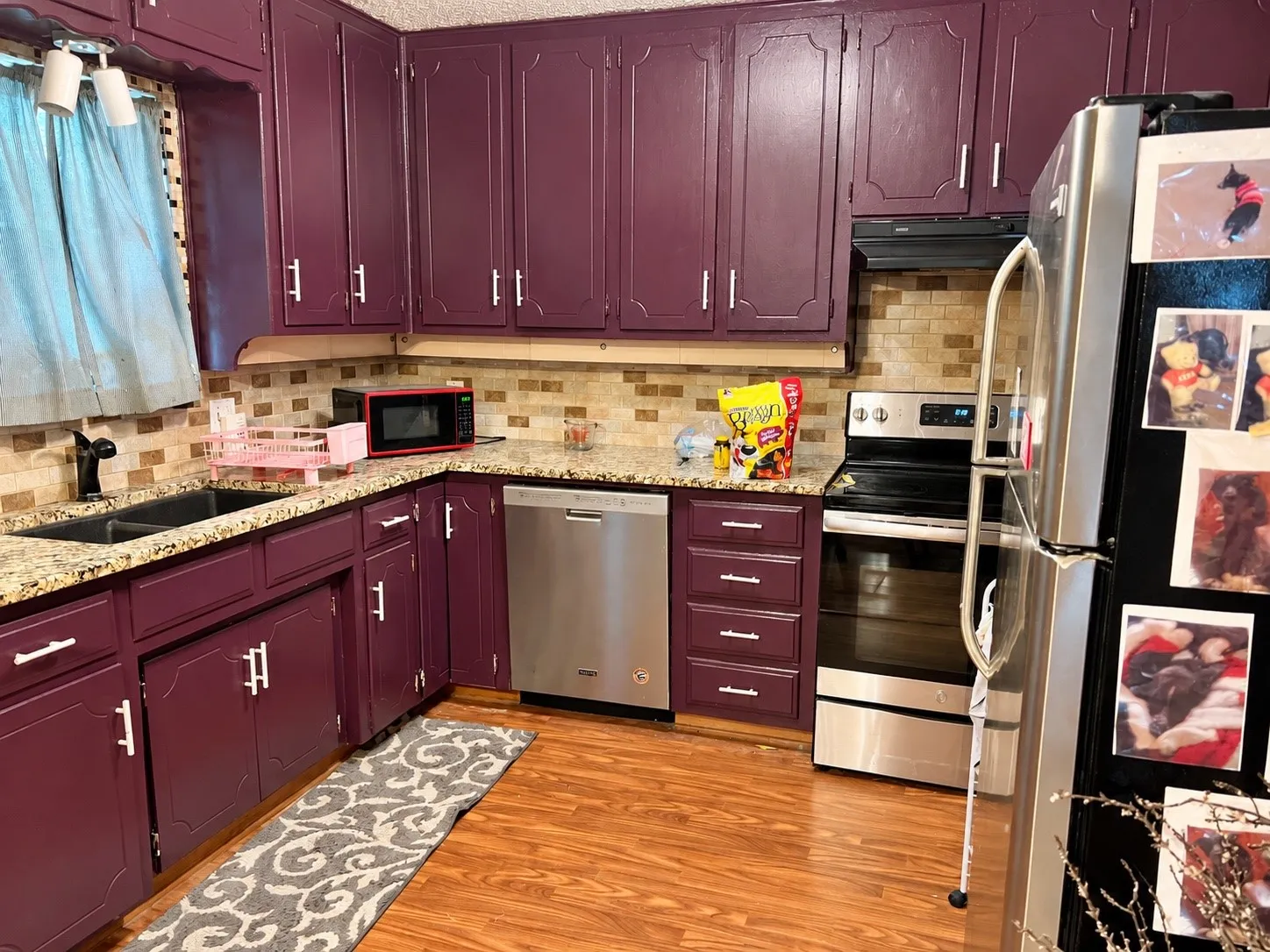 Kitchen featuring rich-toned cabinetry, granite-style countertops, stainless steel appliances, a tiled backsplash, and wood-finish flooring