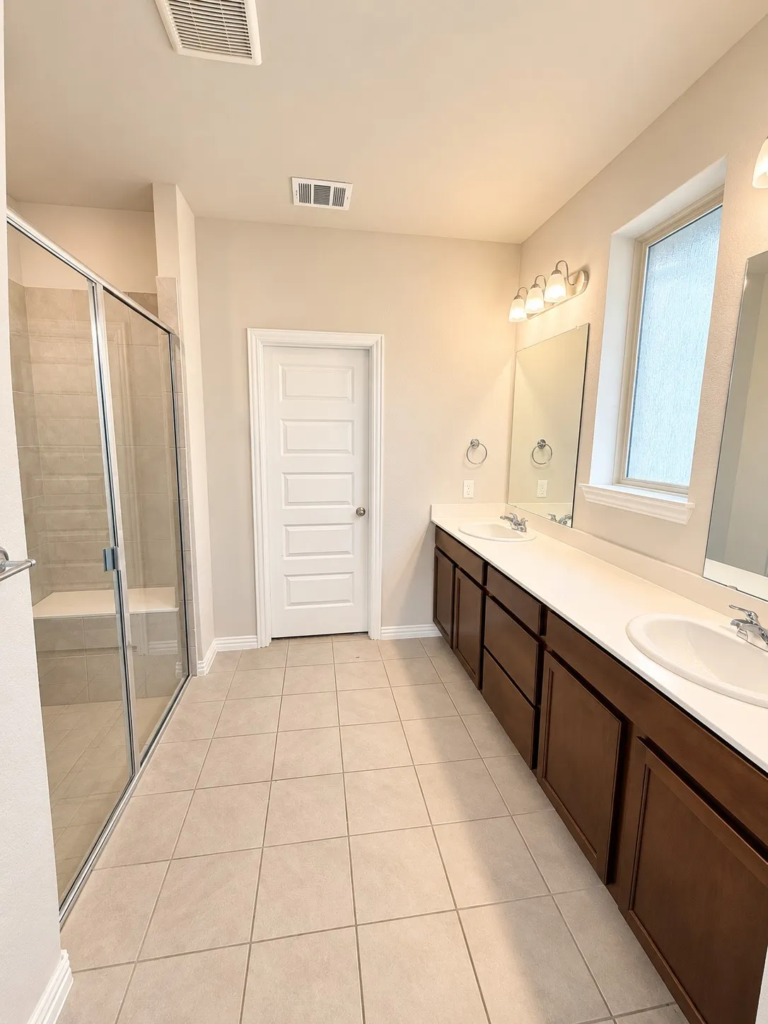 Dual vanity with white undermount sinks, warm wood-finish cabinetry, and neutral tile flooring