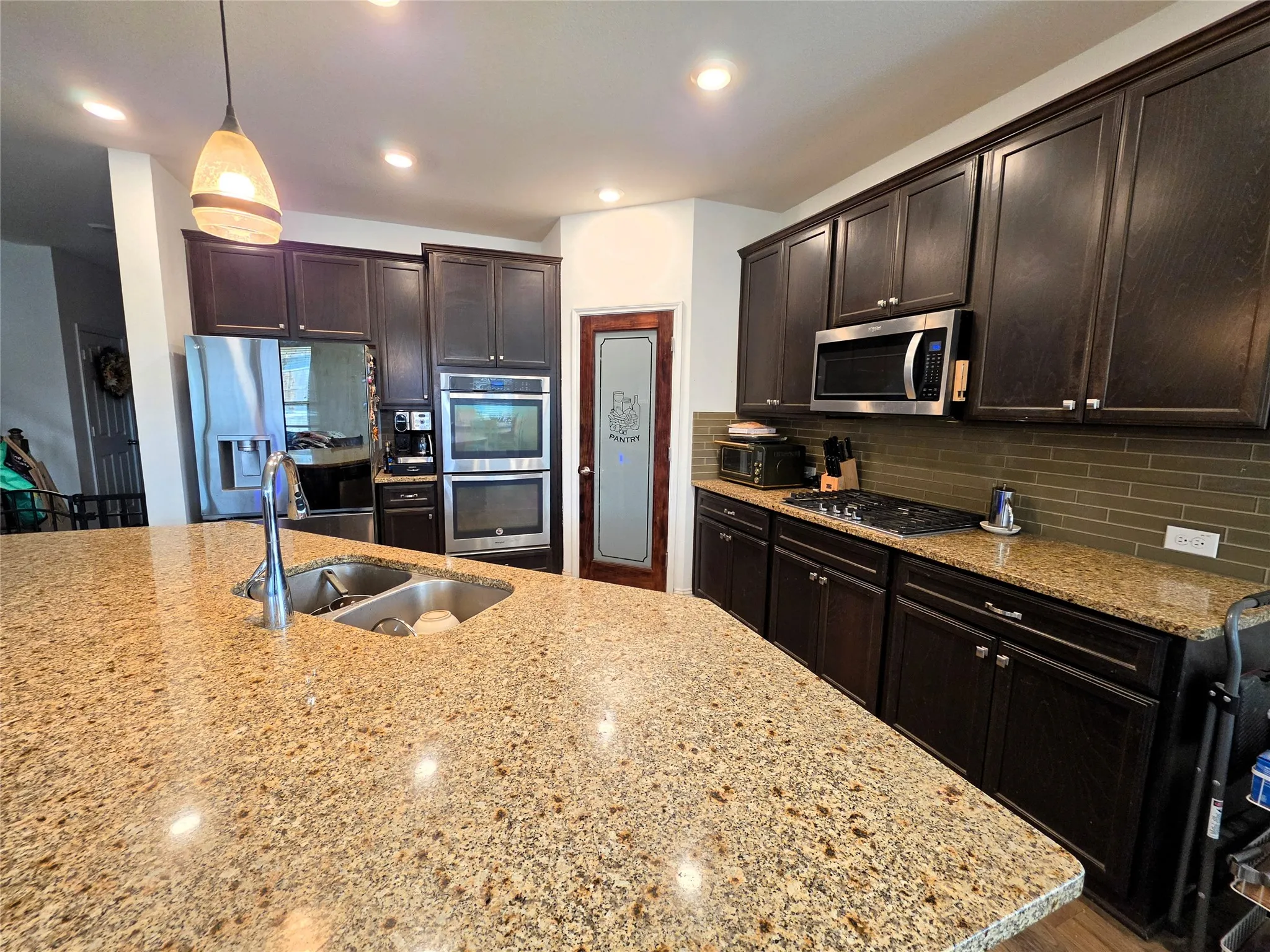 Kitchen featuring an expansive island with a double basin sink, rich wood cabinetry, stainless steel appliances, and a tiled backsplash