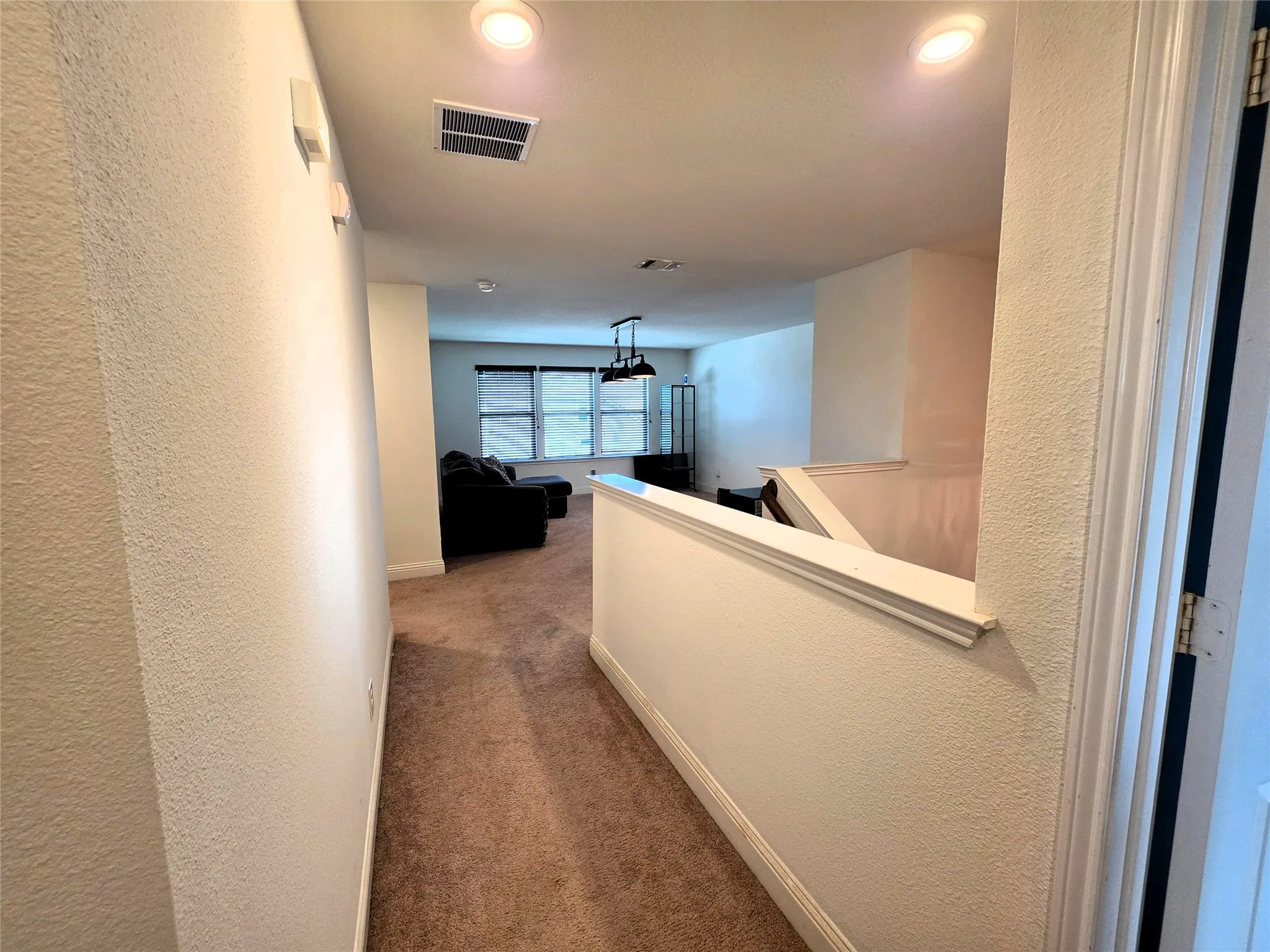 Recessed ceiling lighting, textured walls, carpet flooring, upper-level railing, and window treatments
