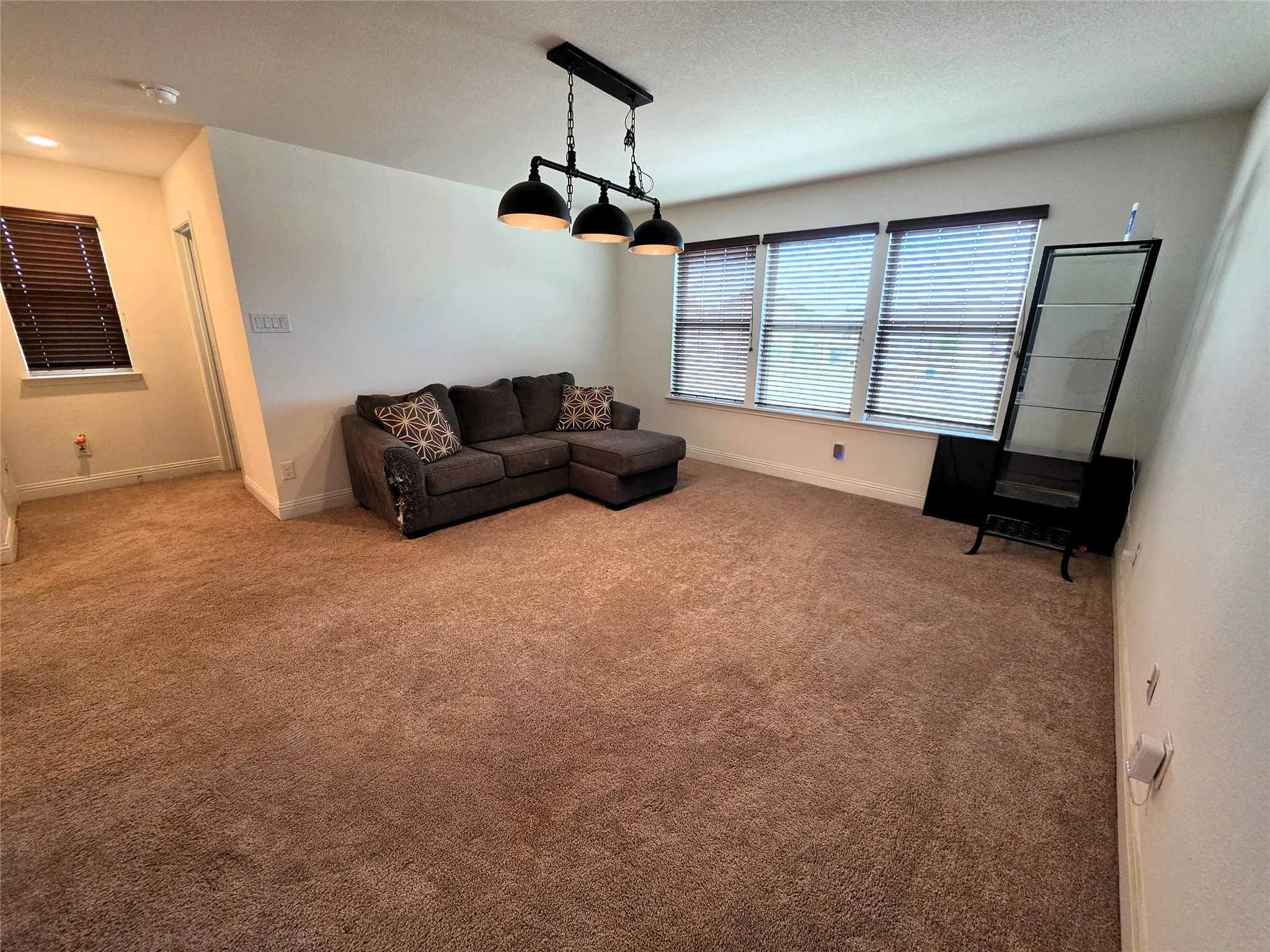 Recessed lighting, triple window with blinds, modern chandelier, brown carpeting, and white wall finishes