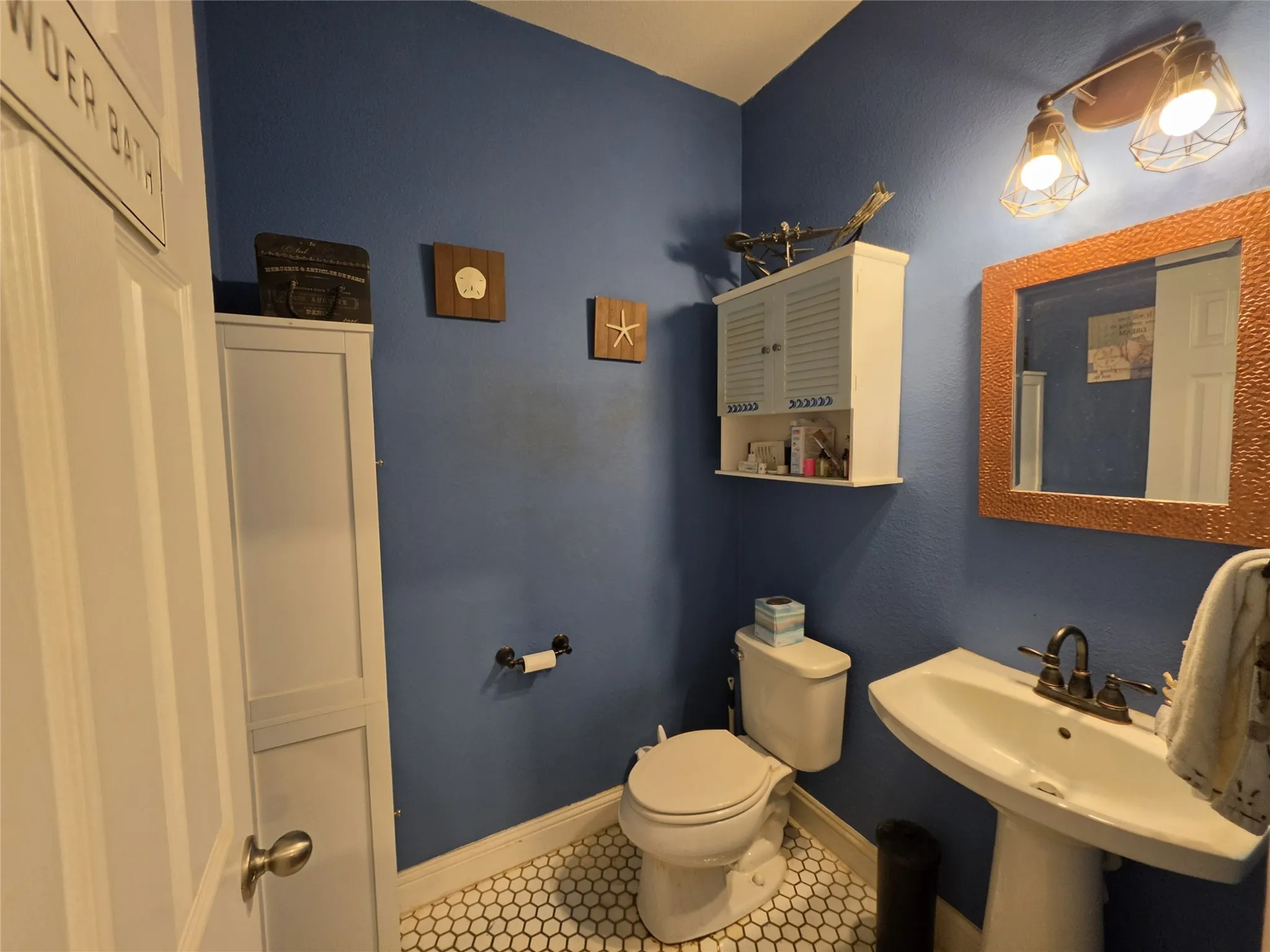 Pedestal sink with dark-toned faucet, wall-mounted light fixture, and honeycomb-patterned floor tiles