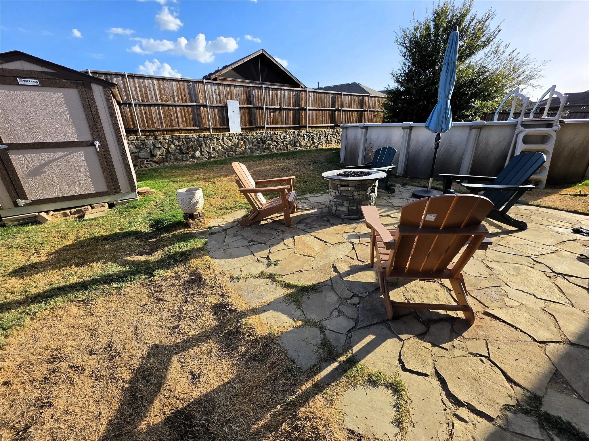Expansive backyard featuring a natural stone patio, wood privacy fence, and a built-in fire pit