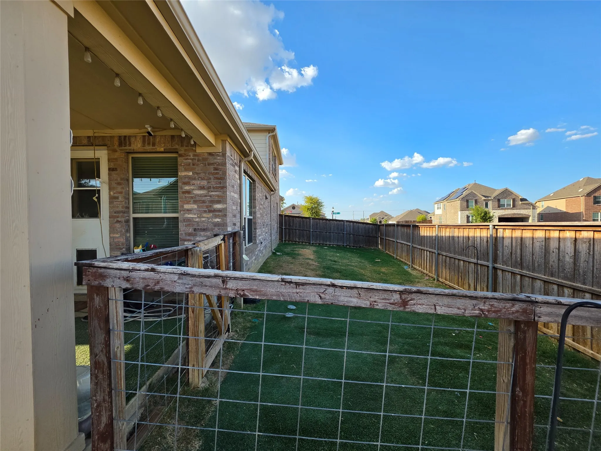 Expansive backyard featuring a manicured lawn, full privacy fencing, and a covered patio with string lighting