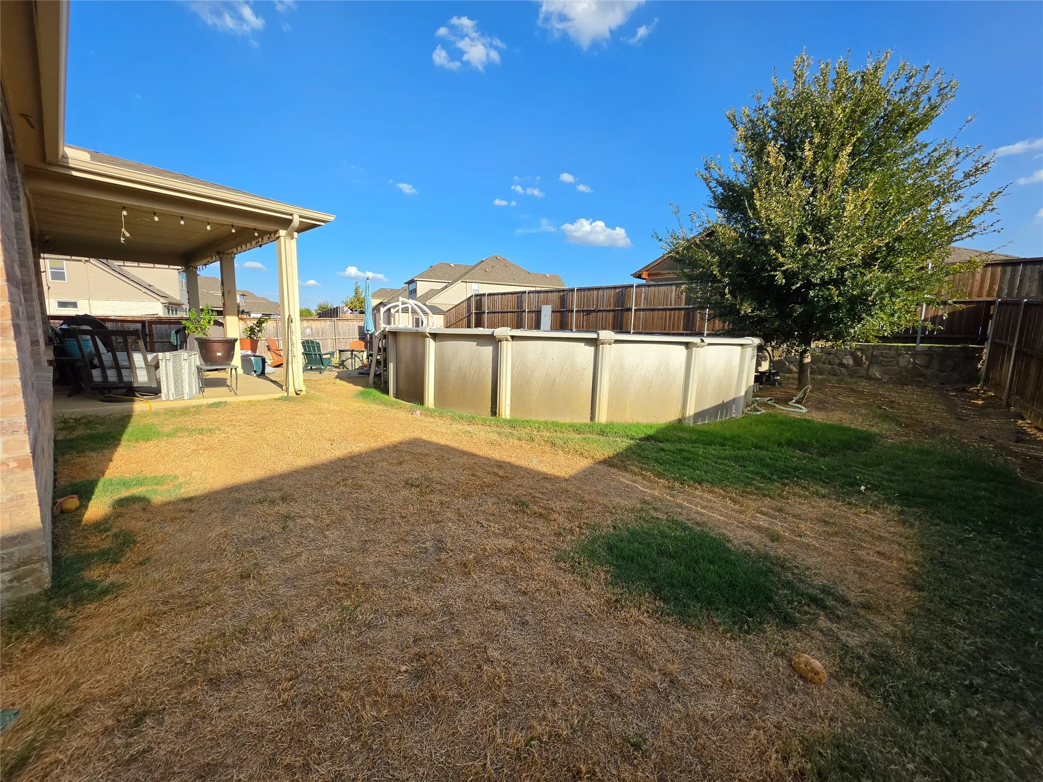 Expansive backyard featuring a covered patio, above-ground pool, mature tree, and privacy fencing