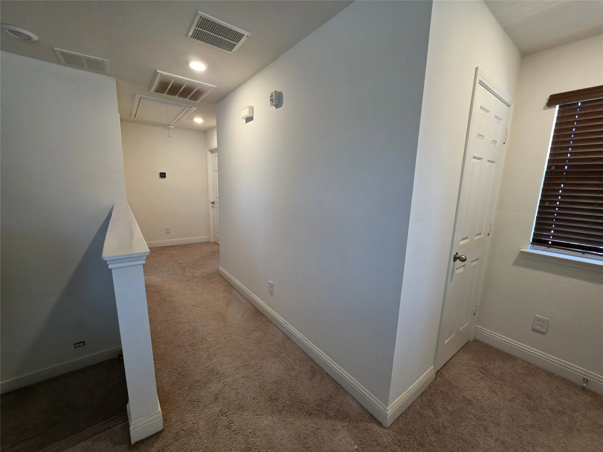 Carpeted hallway featuring recessed lighting, a paneled door, and a window with wood-finish blinds