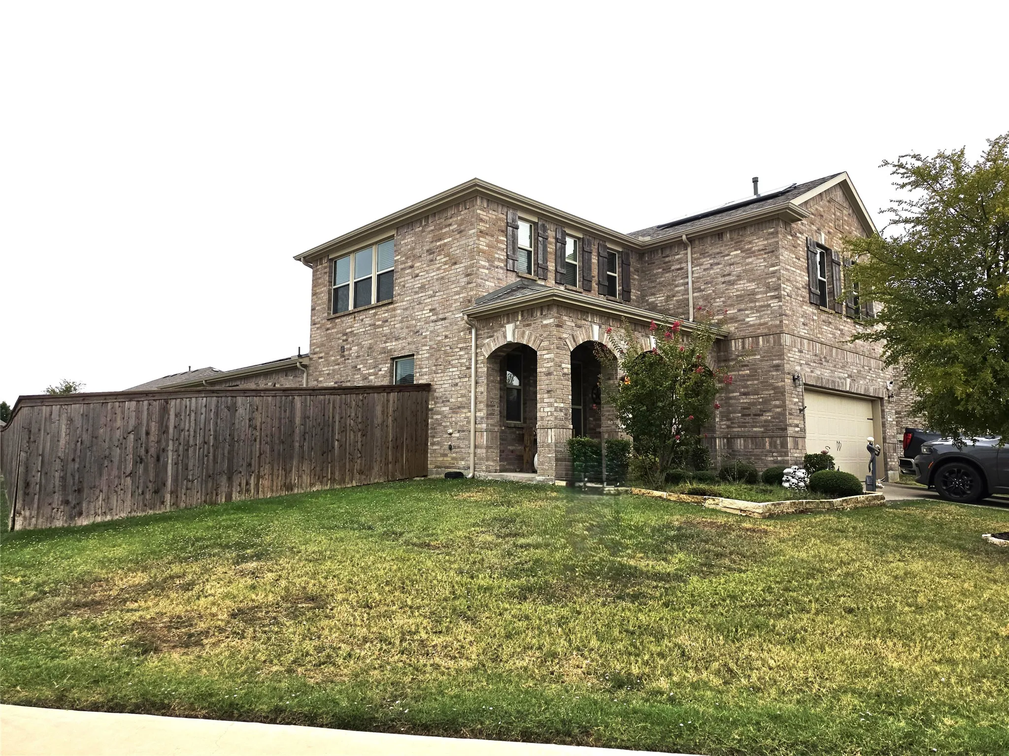 Brick exterior with arched entry, attached garage, and mature landscaping