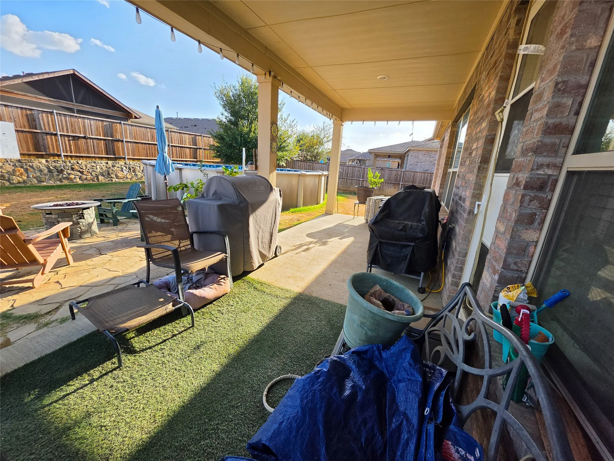 Covered patio featuring string lights, brick exterior, and a simulated grass area