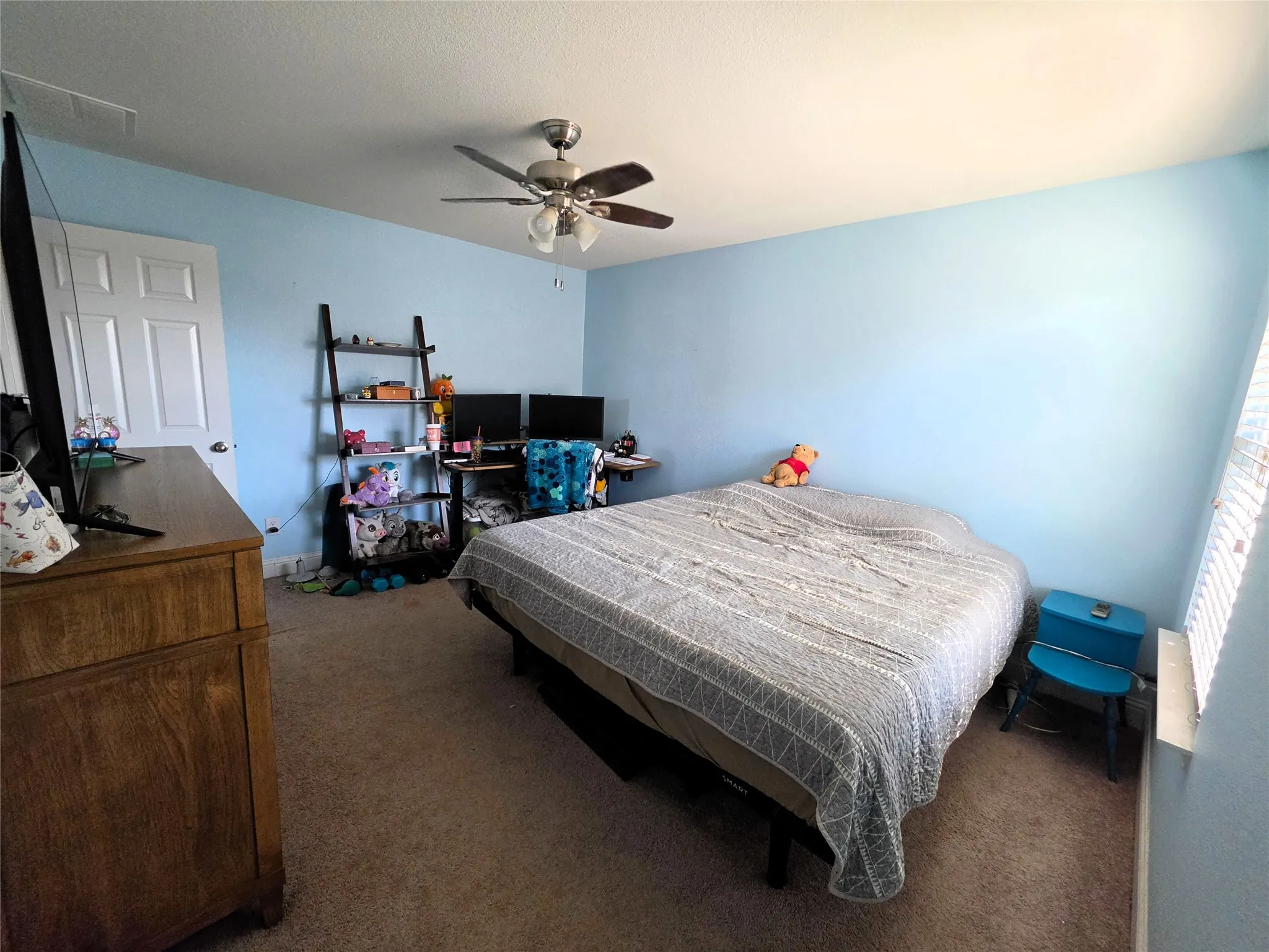 Ceiling fan with light fixture, light blue painted walls, carpeted flooring, and a white paneled door