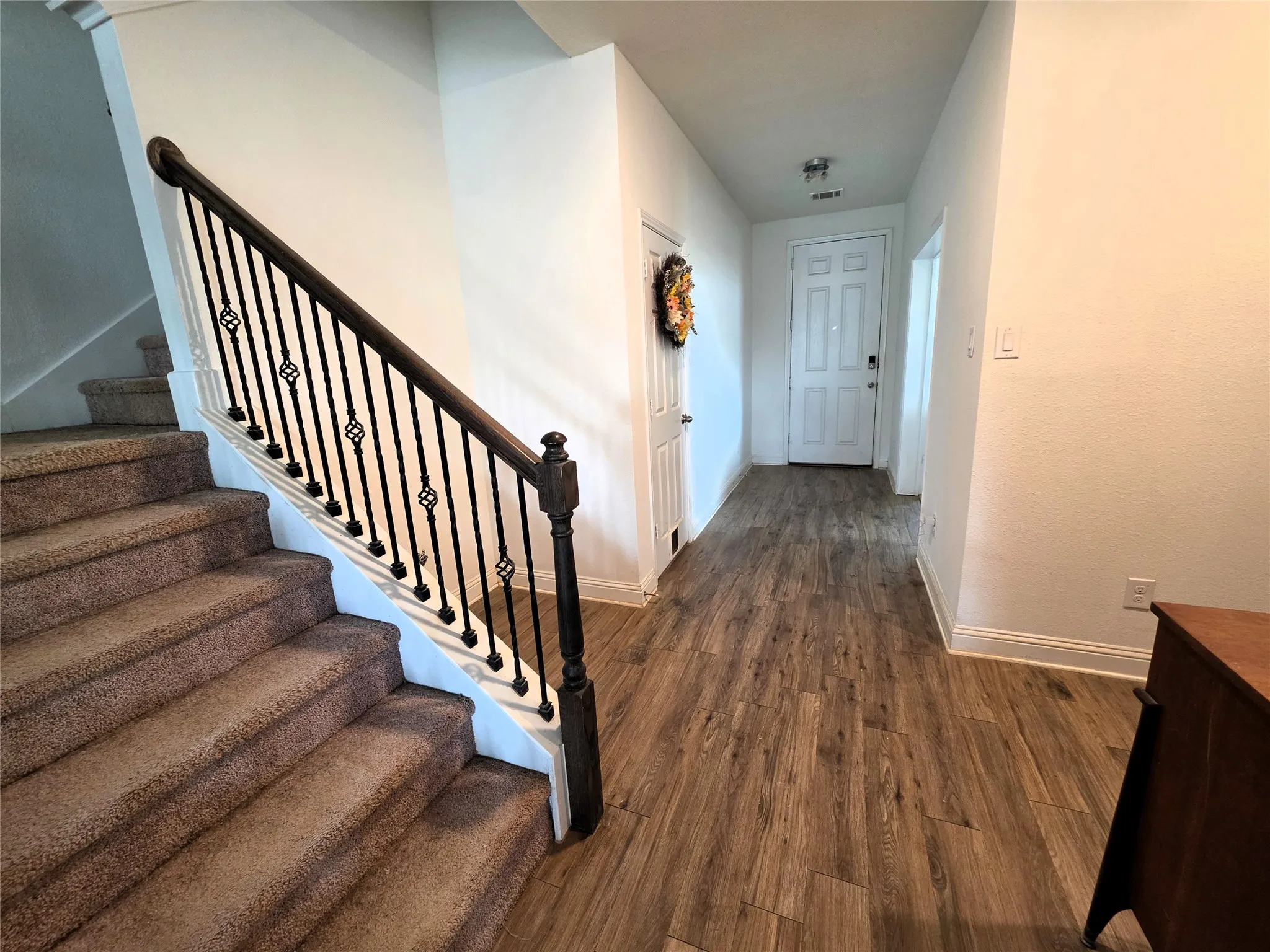 Wood-finish flooring throughout the hallway, leading to a white paneled entry door