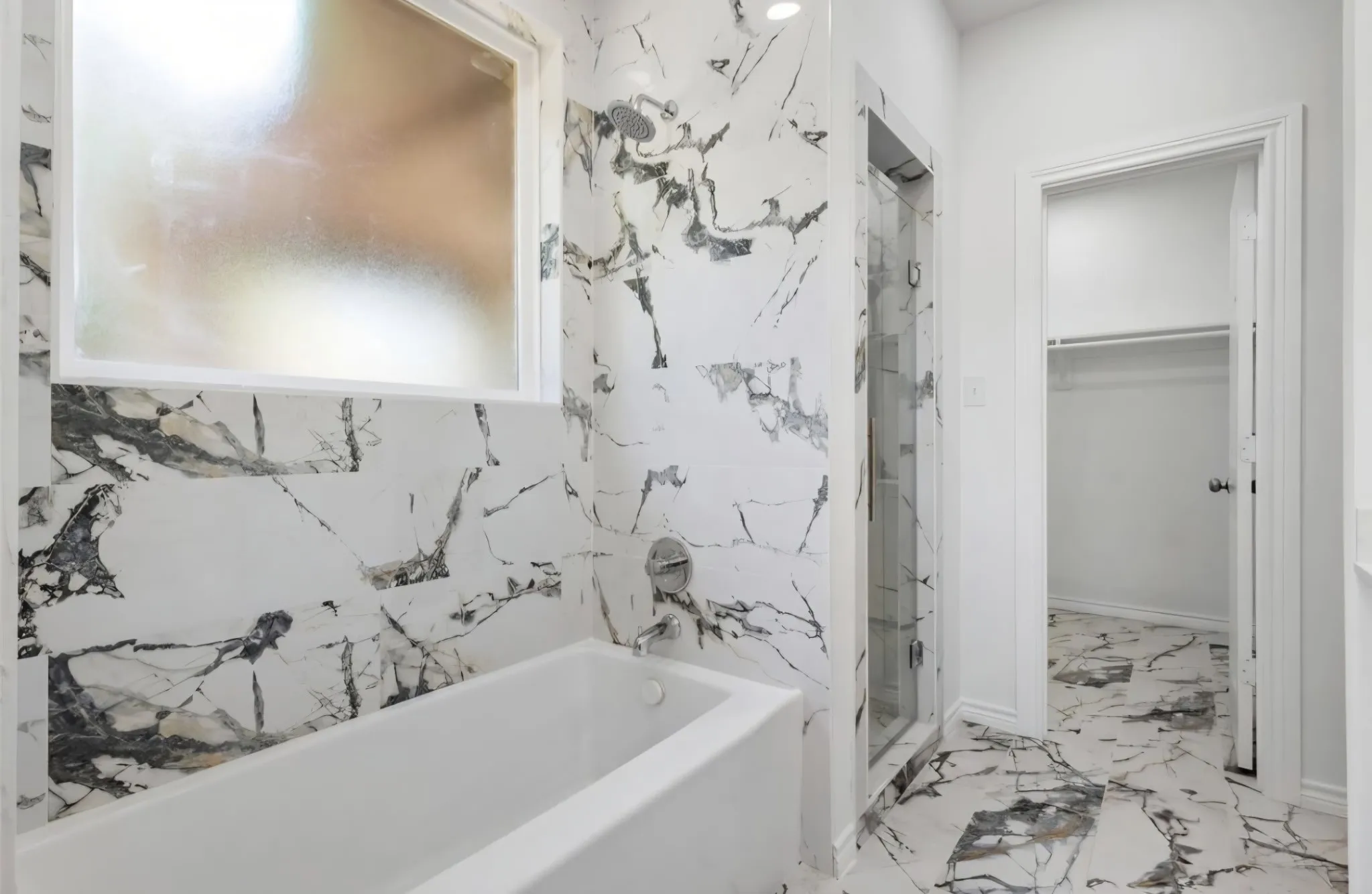 White-tiled bathtub with chrome fixtures, full-height white and grey veined tile surround, and a frosted window