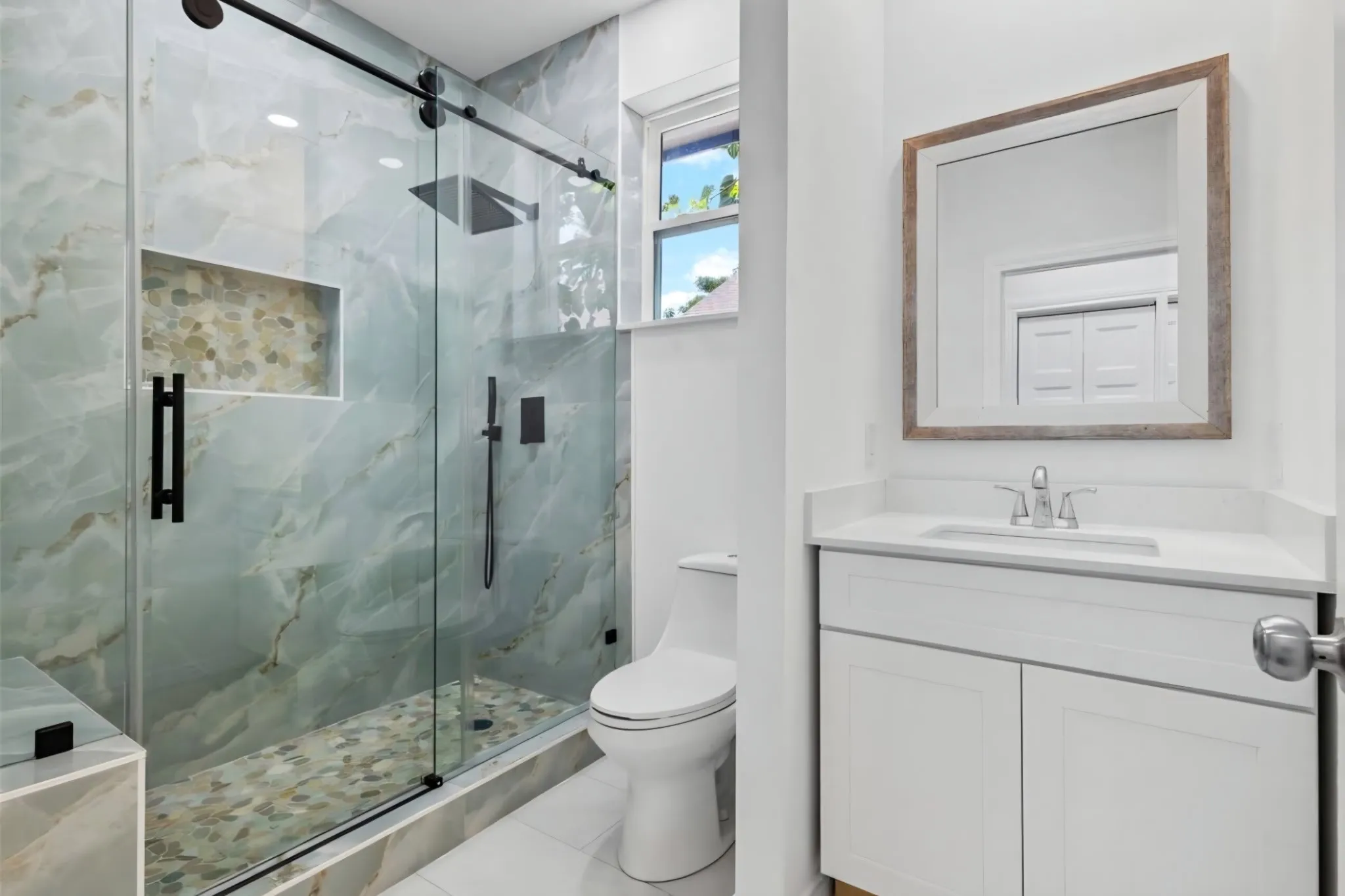 Glass-enclosed shower with a rainfall showerhead, tiled bench, and stone pebble floor