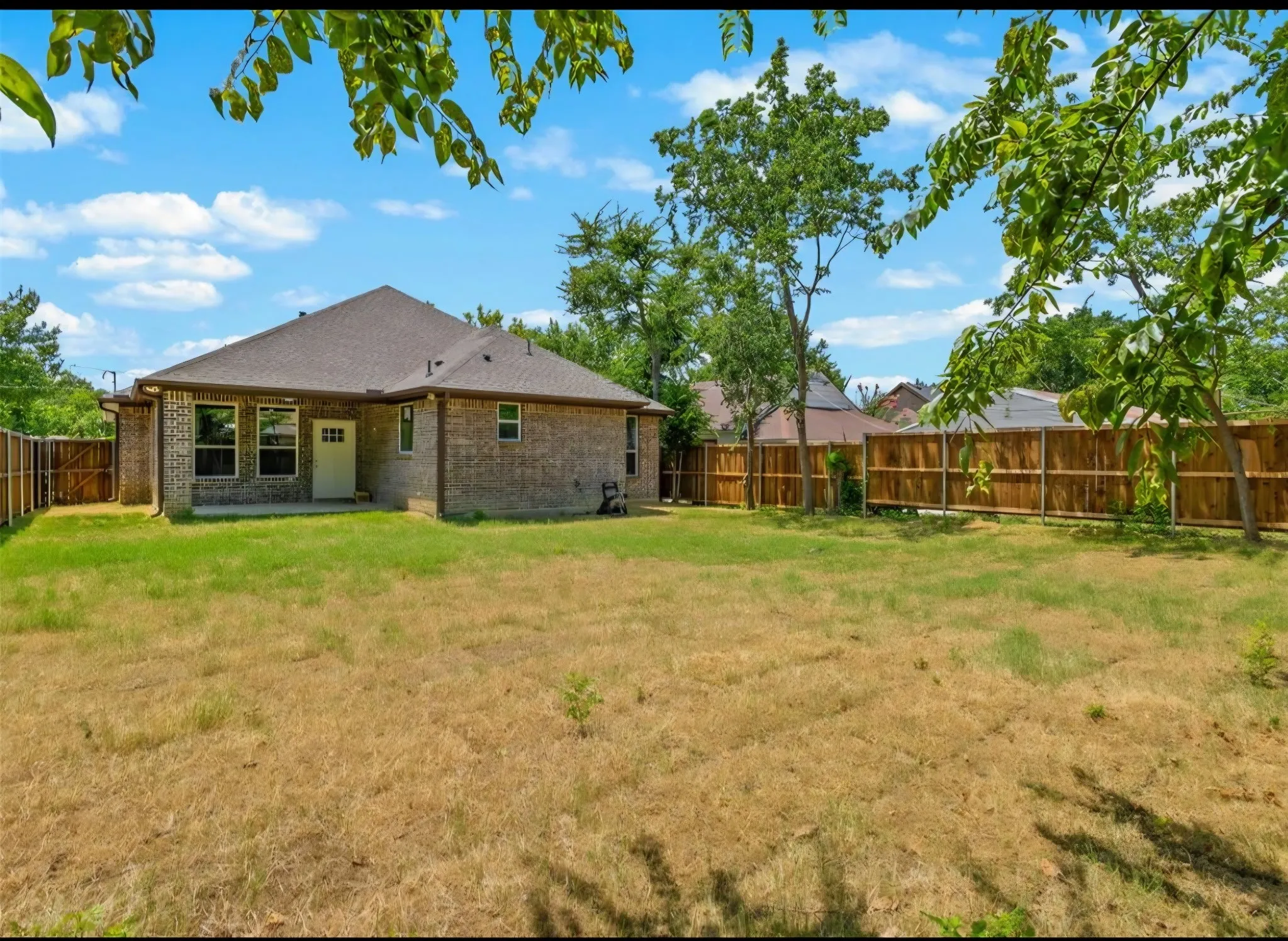 Brick exterior with multiple windows, covered patio, private fencing, and a large yard