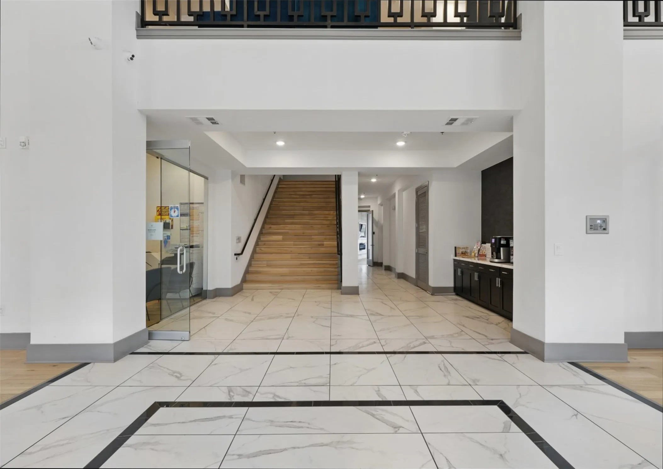 Spacious common area featuring large format marble-look tile flooring with dark accent borders, a wood-finish staircase, and a built-in beverage station