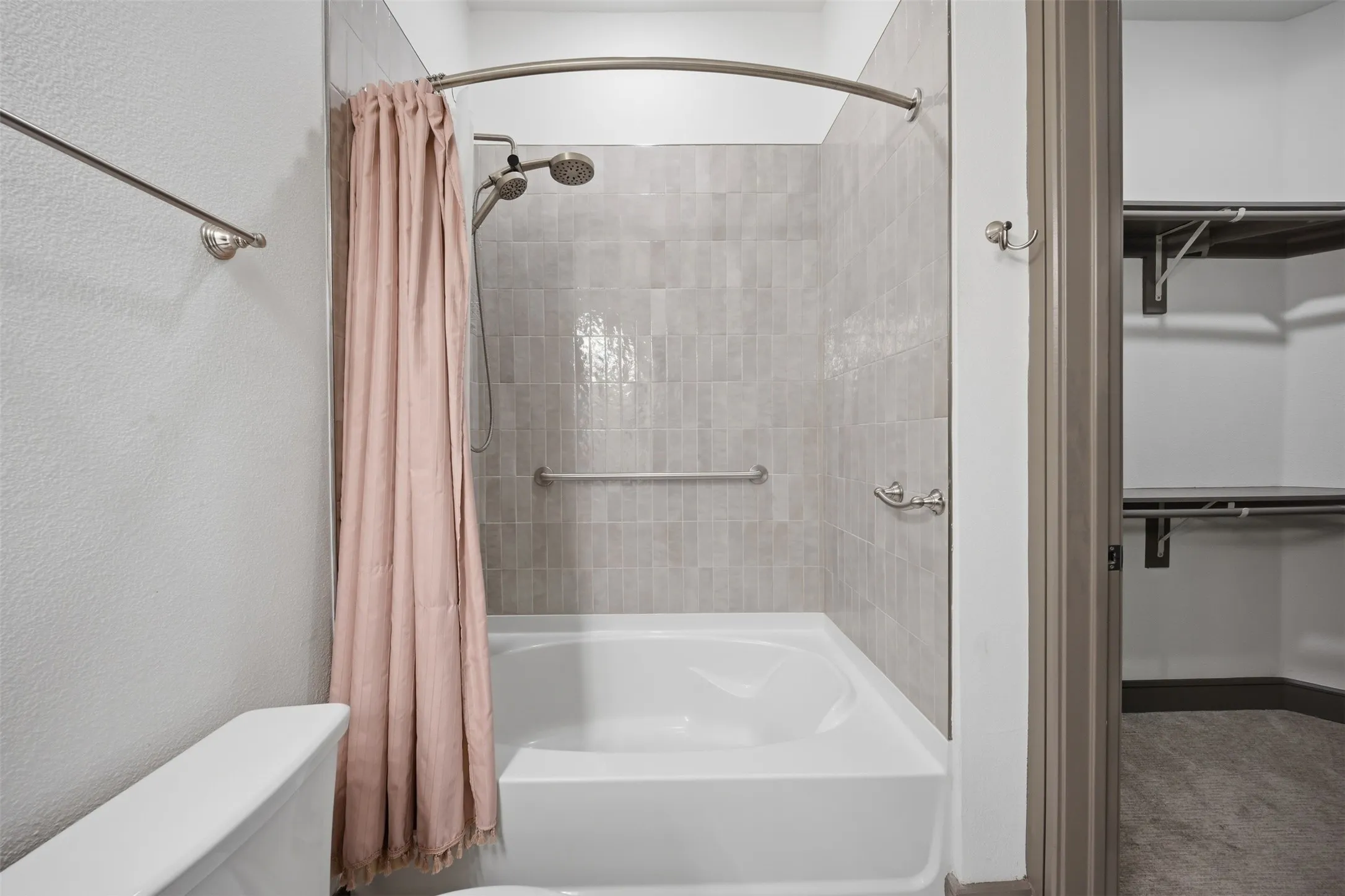 Bathtub with tiled surround, brushed nickel fixtures, and grab bars