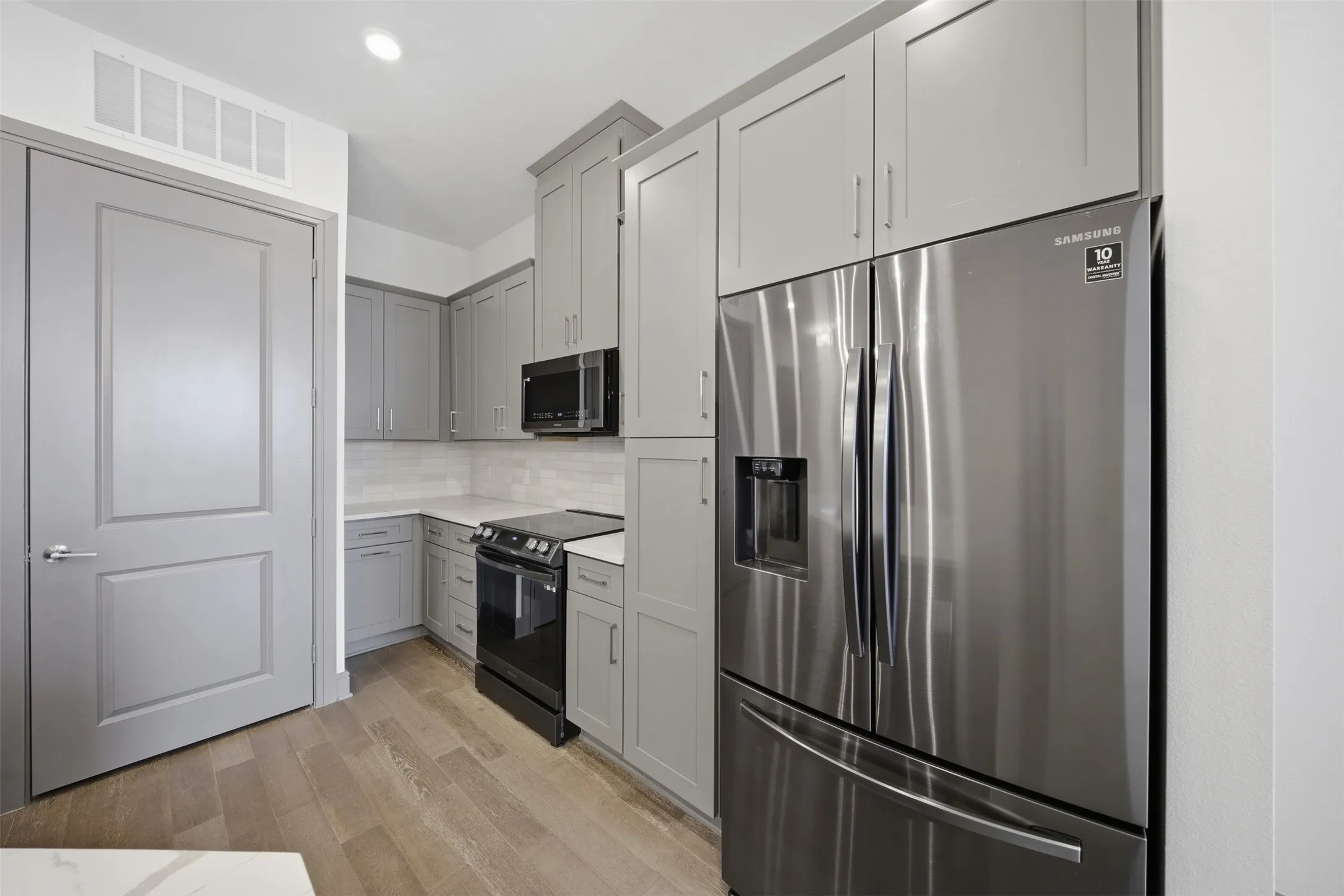 Kitchen featuring light gray cabinetry, stainless steel French door refrigerator, white subway tile backsplash, built-in microwave, and wood-finish flooring