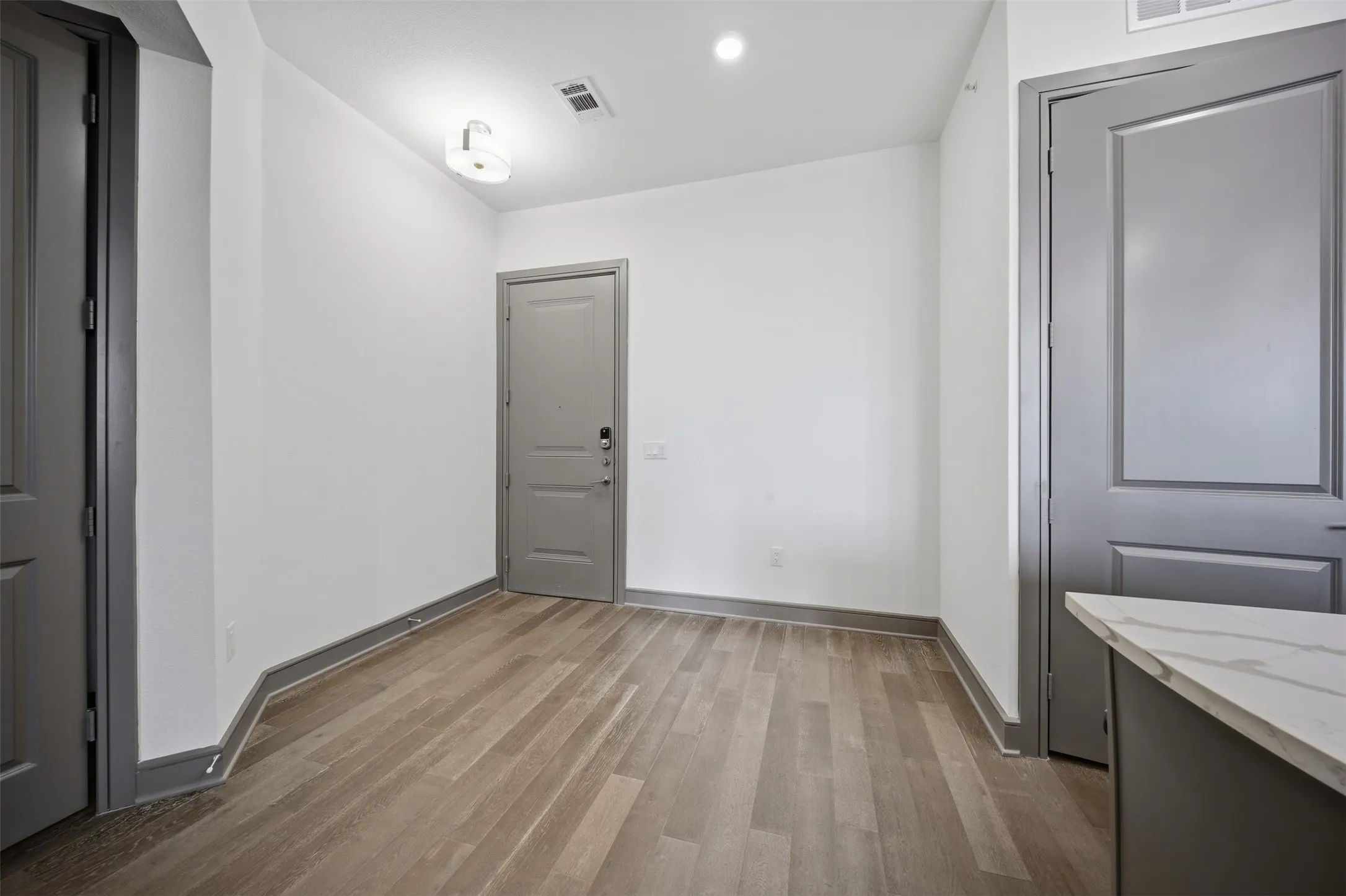Wood-finish flooring, recessed lighting, ceiling-mounted light fixture, white walls, and gray trim