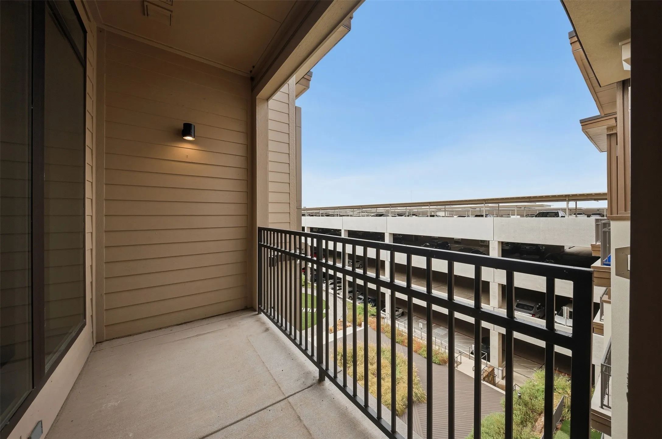 Private balcony with concrete flooring, black metal railing, and exterior wall sconce