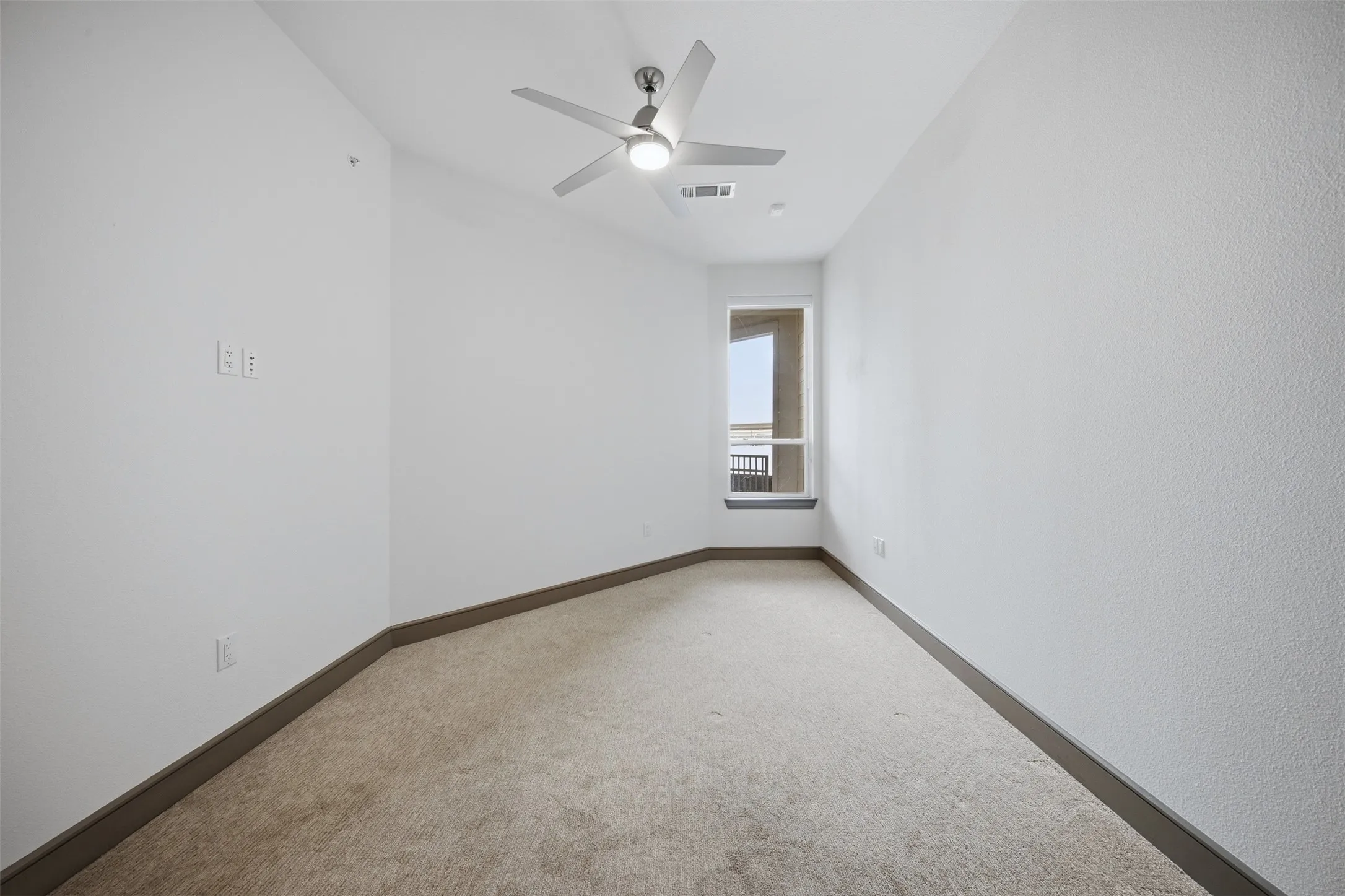 Angled wall with single window, ceiling fan, and light-colored carpet