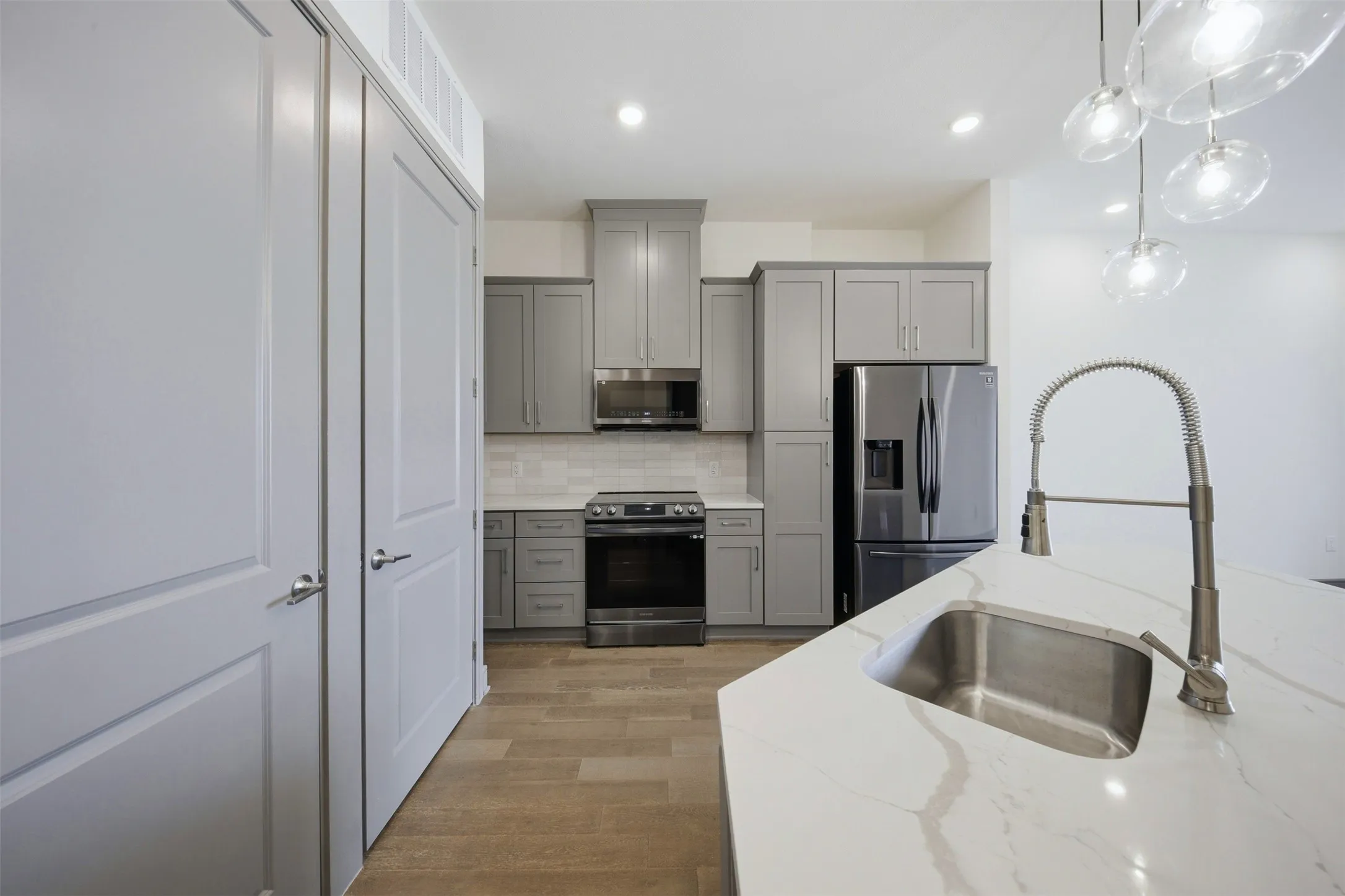 Kitchen featuring a stainless steel sink, pull-down faucet, light countertops, gray cabinetry, and wood-finish flooring