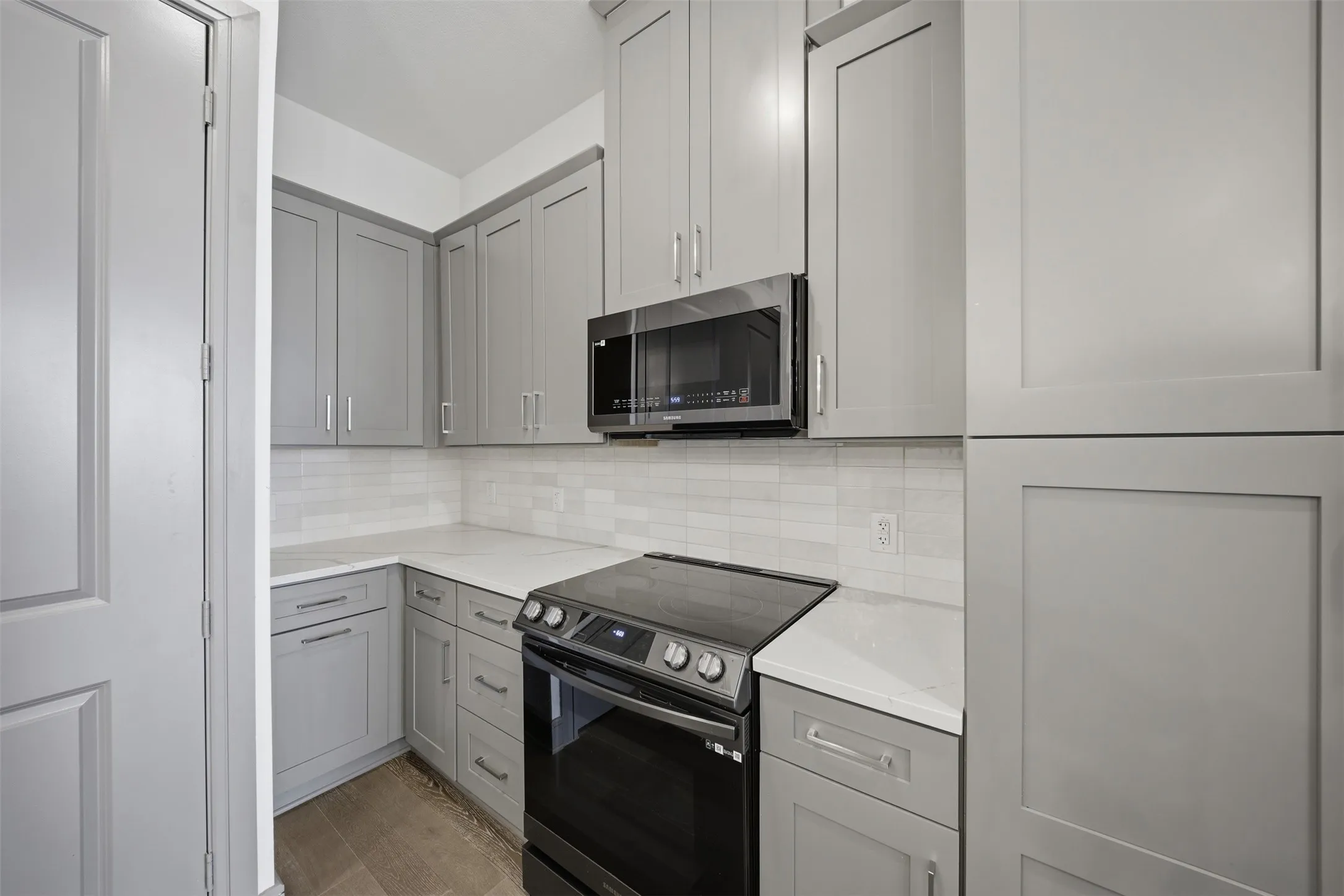 Grey shaker-style cabinetry, white subway tile backsplash, white countertops, built-in microwave, and an electric range