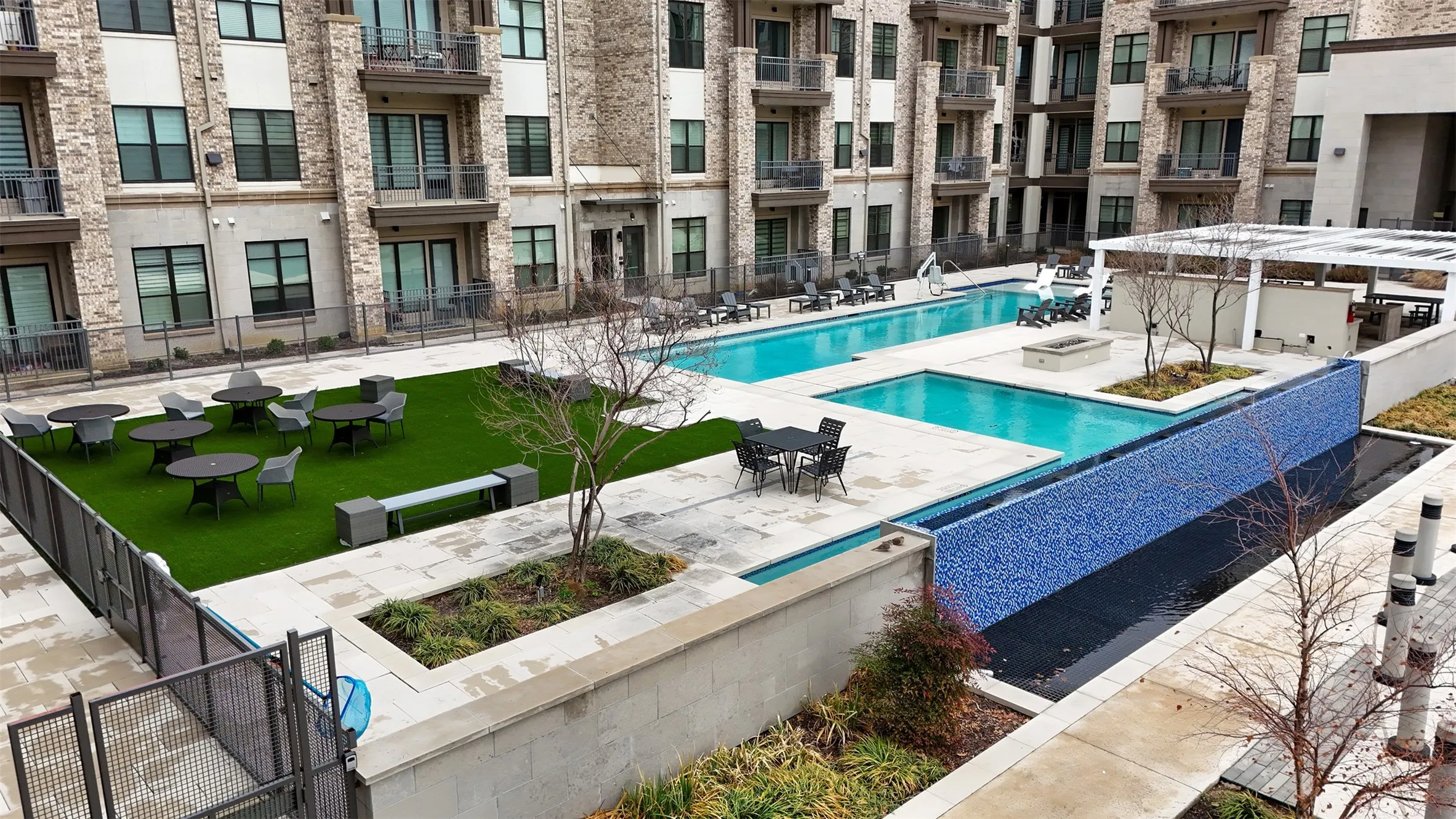 Courtyard featuring multiple swimming pools, a mosaic-tiled water feature, artificial turf recreation areas, and a stone-clad building exterior