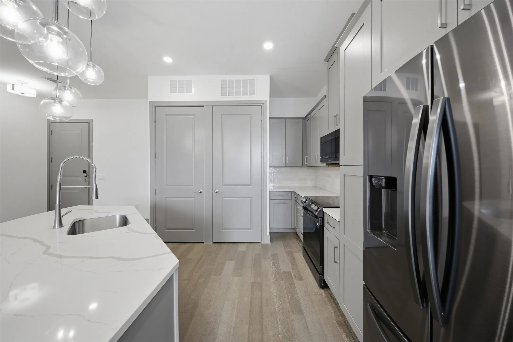 Modern kitchen featuring a stainless steel sink, sleek counter surfaces, wood-finish flooring, contemporary cabinetry, and integrated appliances
