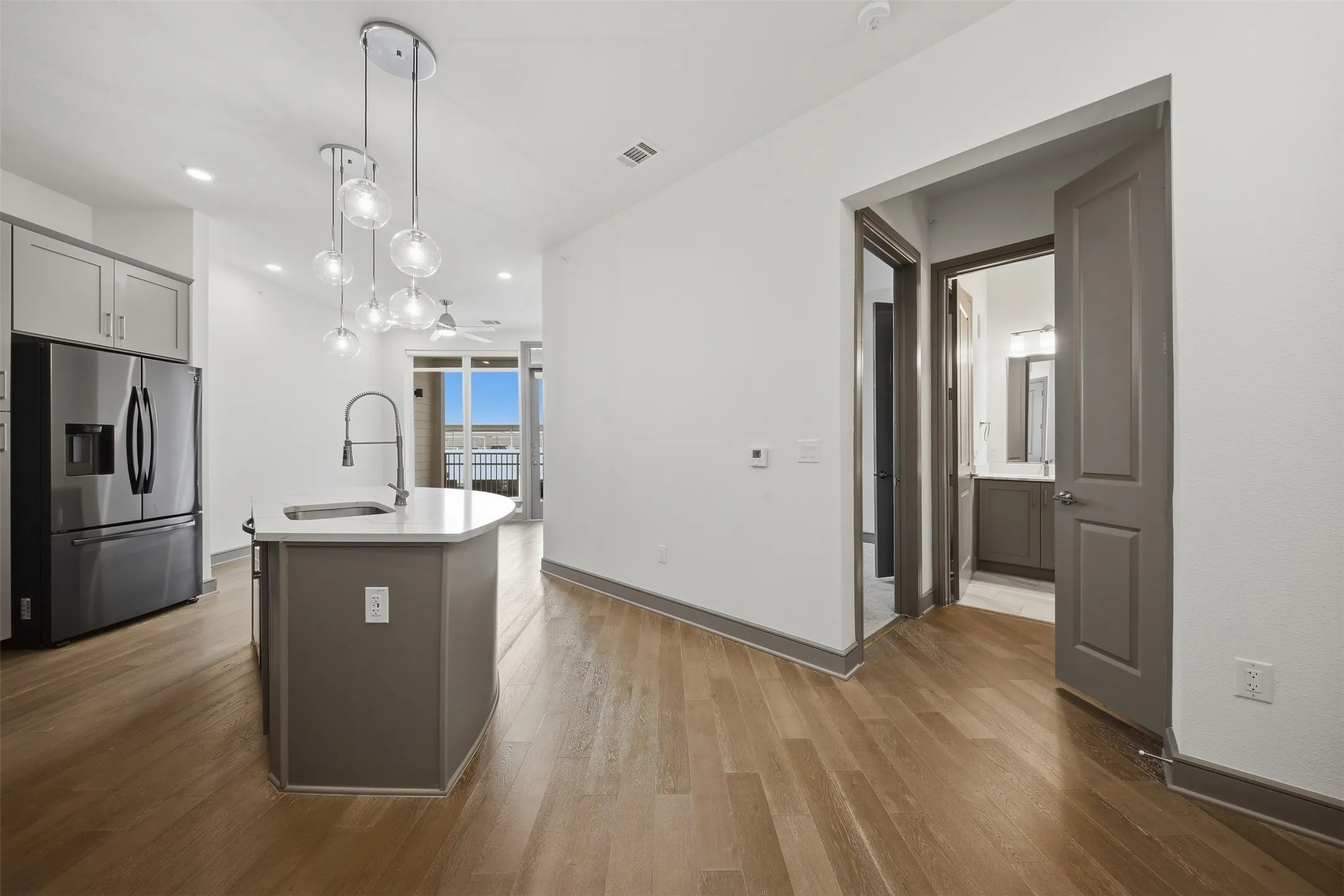 Kitchen island with a white countertop and undermount sink, stainless steel refrigerator, wood-finish flooring, and a multi-pendant light fixture