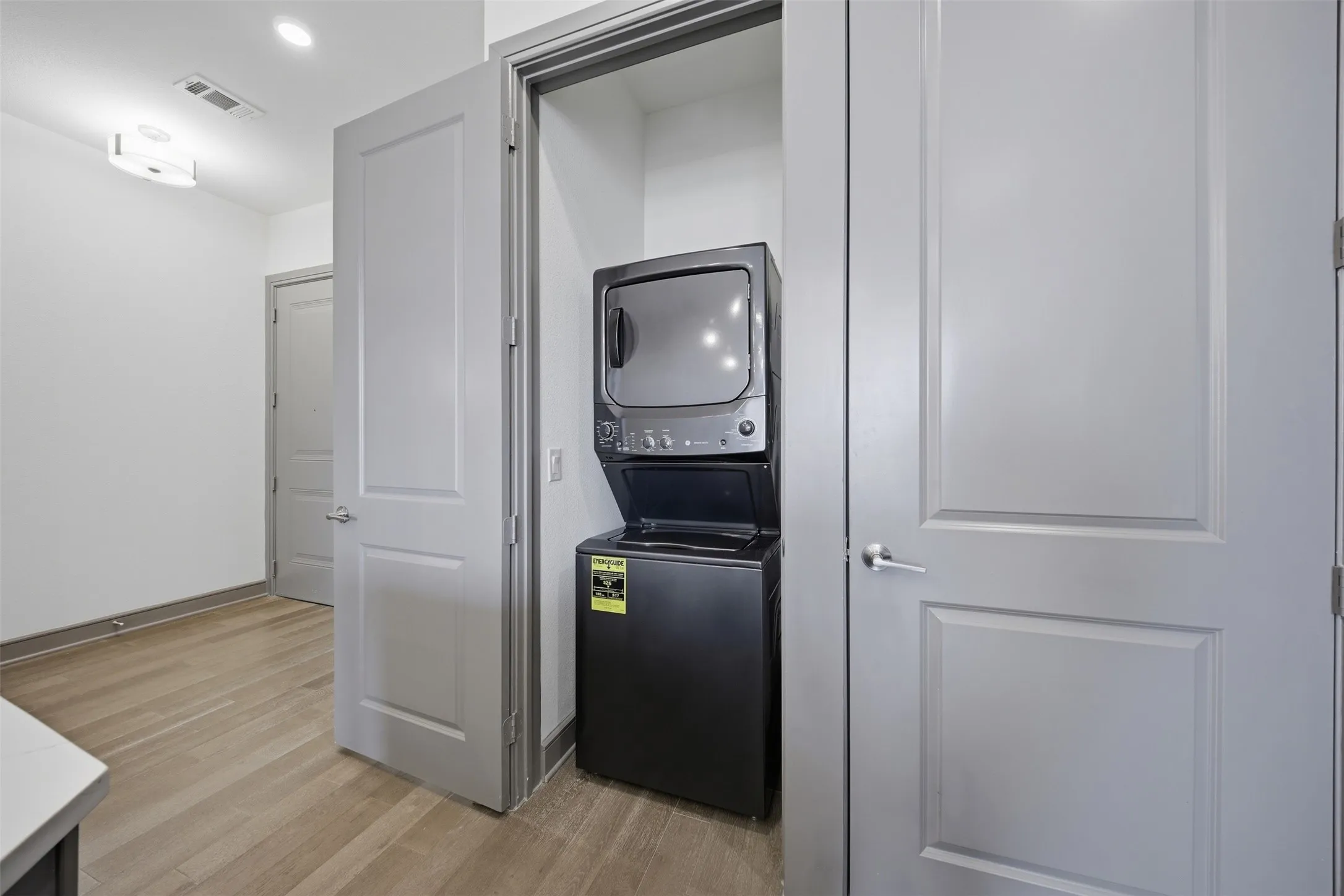 Stacked washer and dryer unit, light wood-finish flooring, white walls, and contemporary light fixture