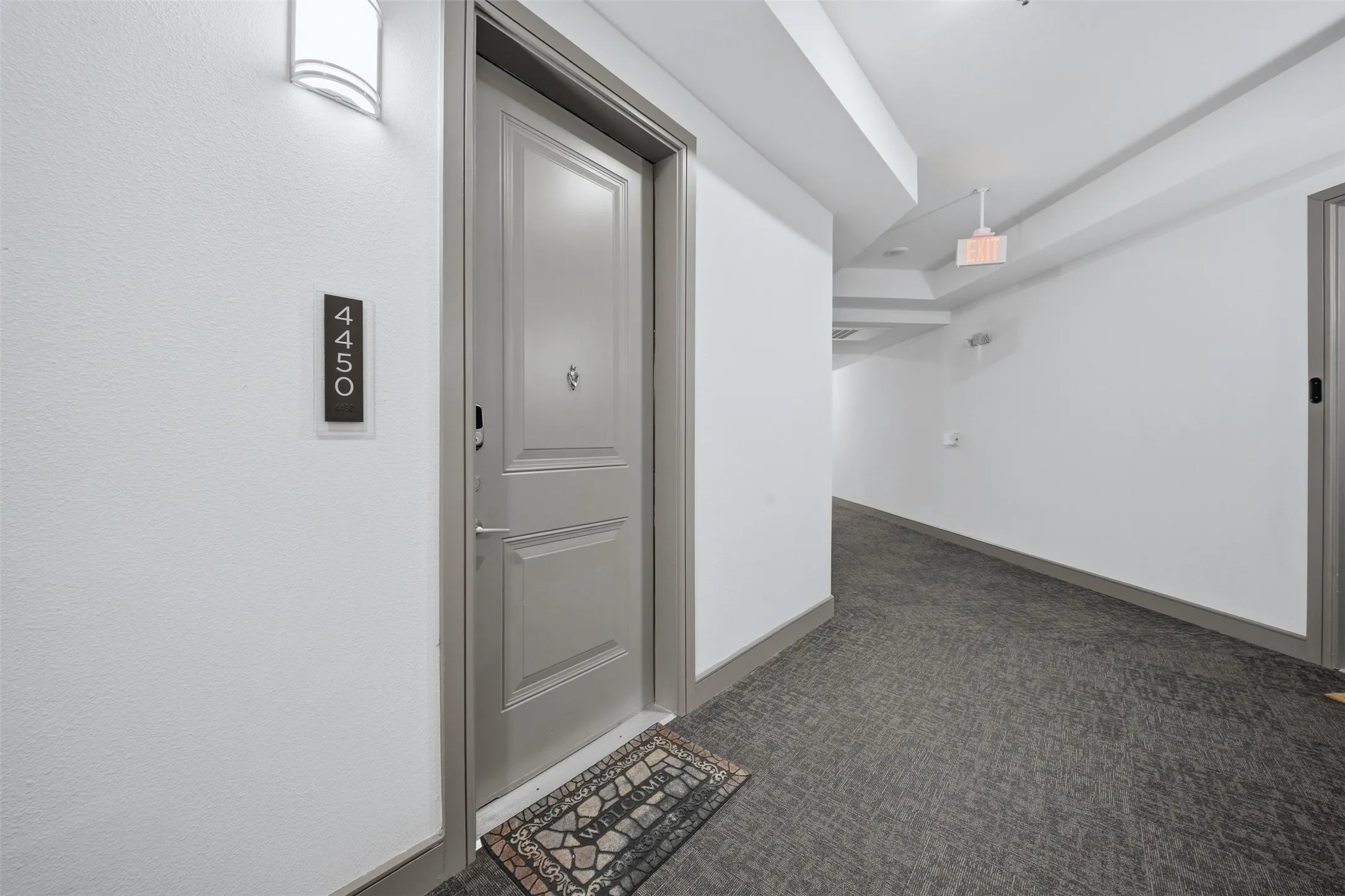 Entry door with paneling, modern wall sconce, and textured carpeting in the hallway