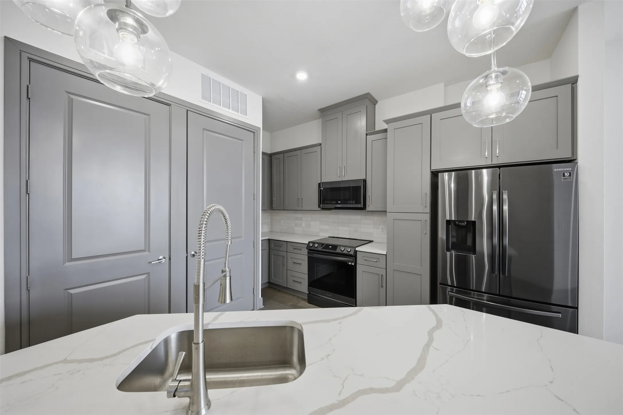 Kitchen featuring a stainless steel sink, large kitchen island with a stone countertop, grey cabinetry, stainless steel appliances, and a tile backsplash