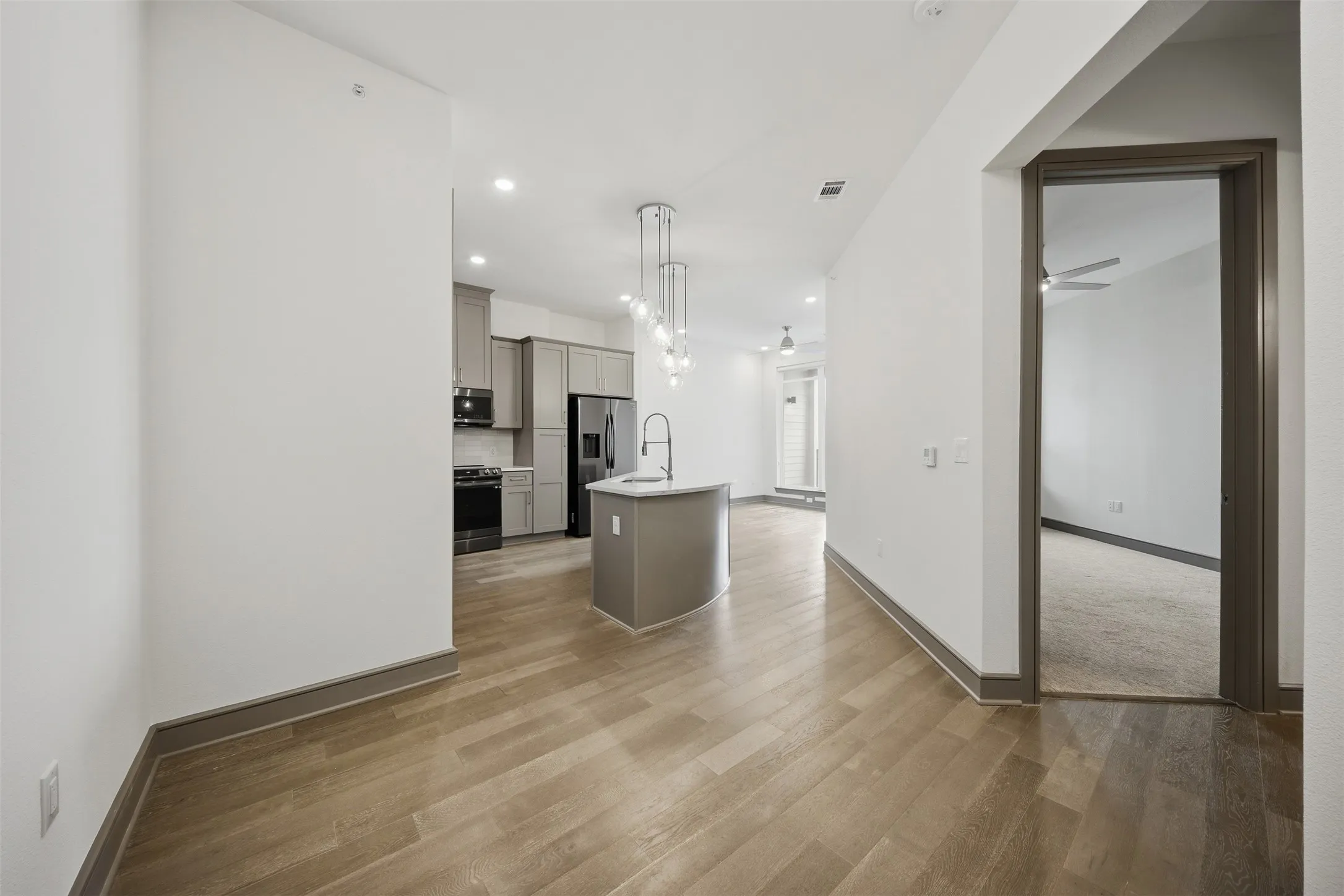 Open-concept kitchen with light wood-finish flooring, gray cabinetry, a central island, and recessed lighting