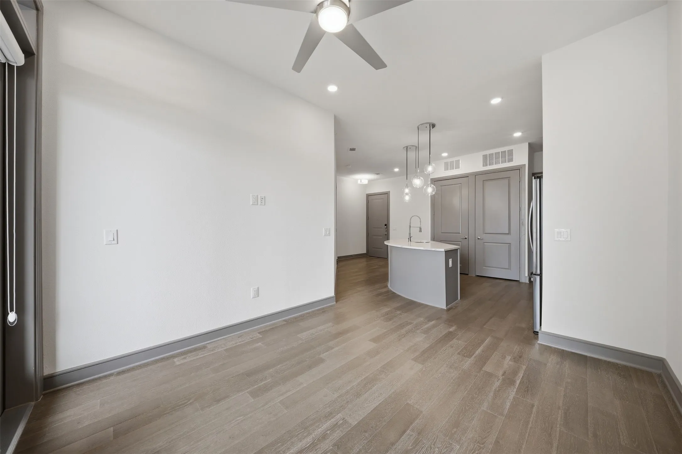 Wood-finish flooring, recessed lighting, ceiling fan, curved kitchen island with pendant lighting, and stainless steel refrigerator