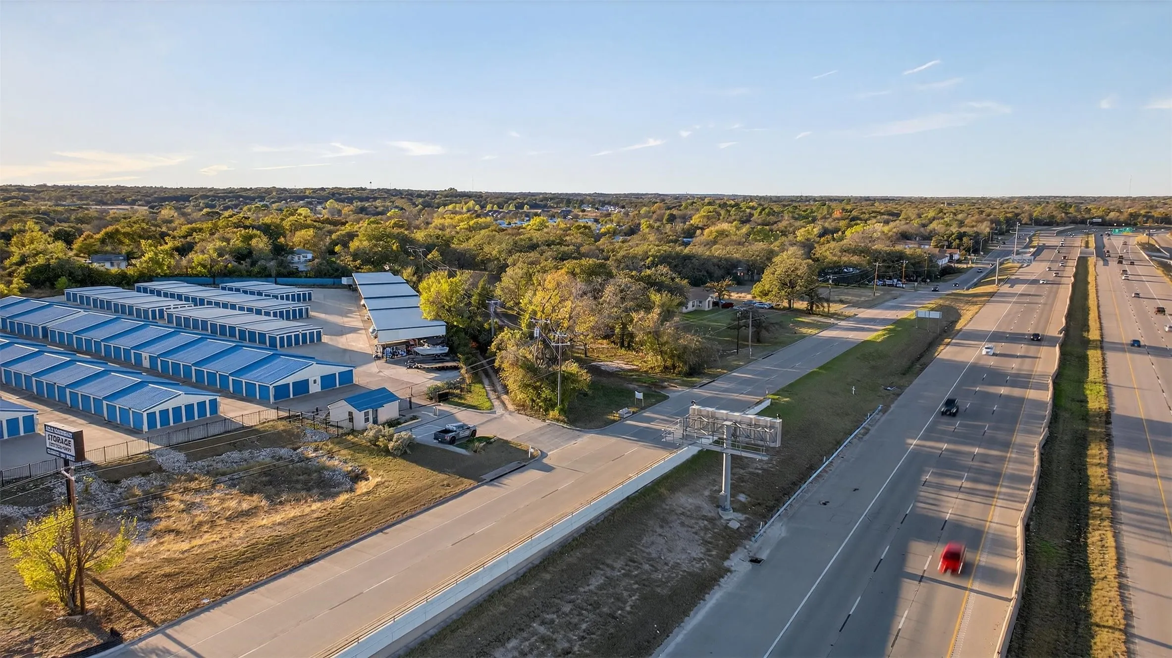 Multiple rows of storage units with blue doors, a detached office building, and paved driveways